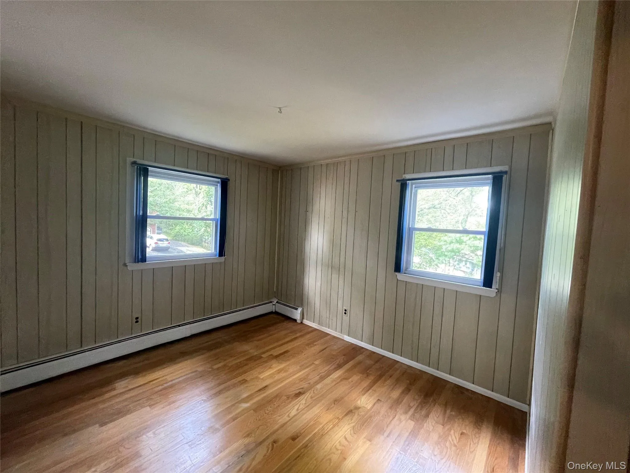 Spare room with light wood-style floors, a baseboard radiator, plenty of natural light, and wood walls Spare room with light wood-style floors, a baseboard radiator, plenty of natural light, and wood walls