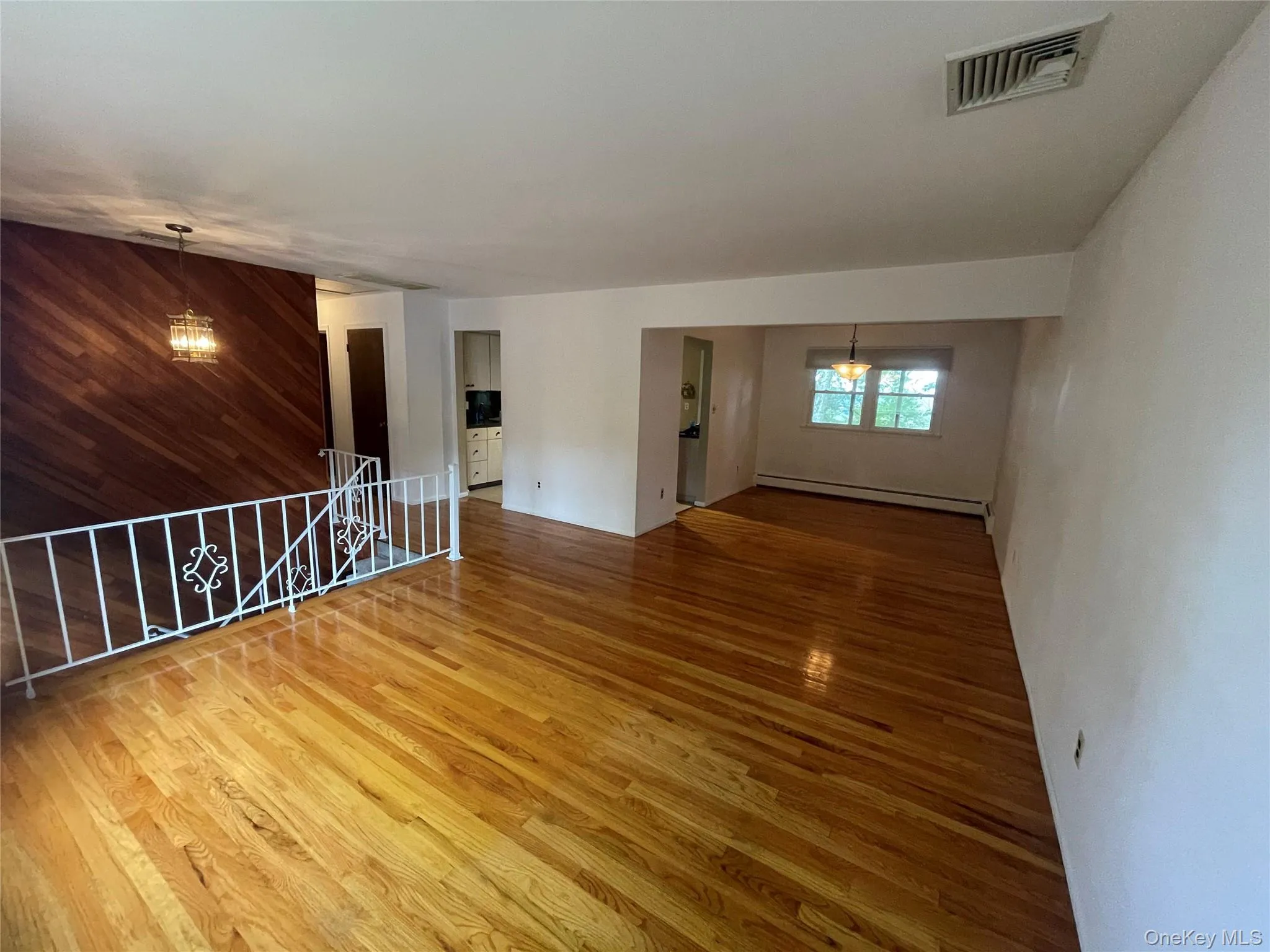 Empty room with a chandelier, wood finished floors, a baseboard heating unit, and wooden walls Empty room with a chandelier, wood finished floors, a baseboard heating unit, and wooden walls