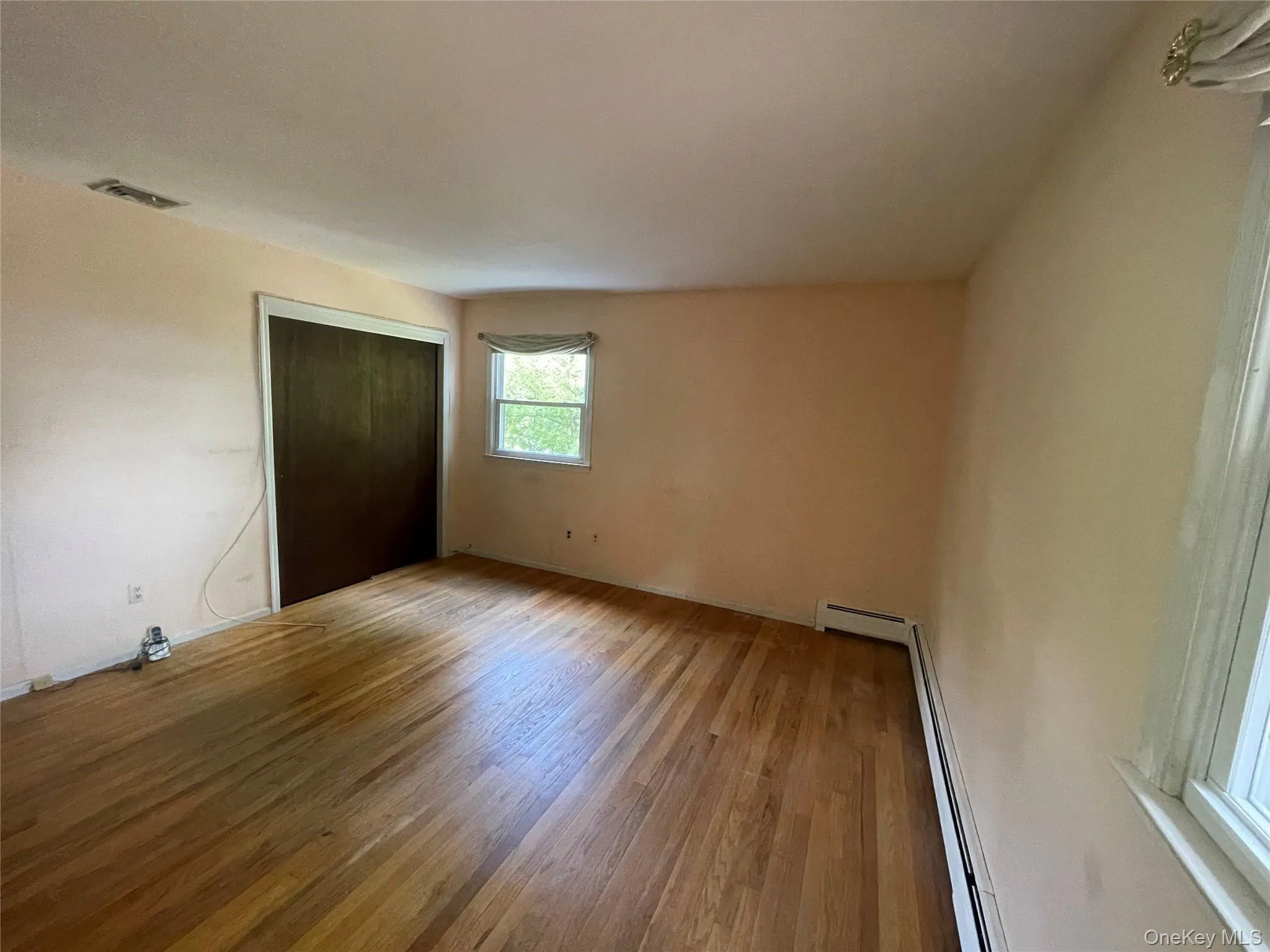 Unfurnished bedroom featuring wood finished floors, a closet, and a baseboard heating unit Unfurnished bedroom featuring wood finished floors, a closet, and a baseboard heating unit