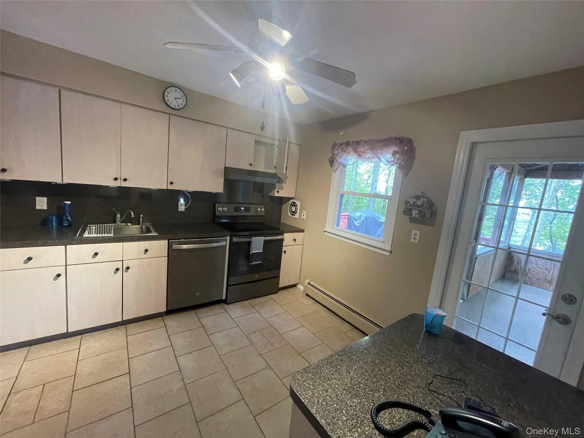Kitchen featuring appliances with stainless steel finishes, a baseboard radiator, light tile patterned floors, under cabinet range hood, and ceiling fan Kitchen featuring appliances with stainless steel finishes, a baseboard radiator, light tile patterned floors, under cabinet range hood, and ceiling fan