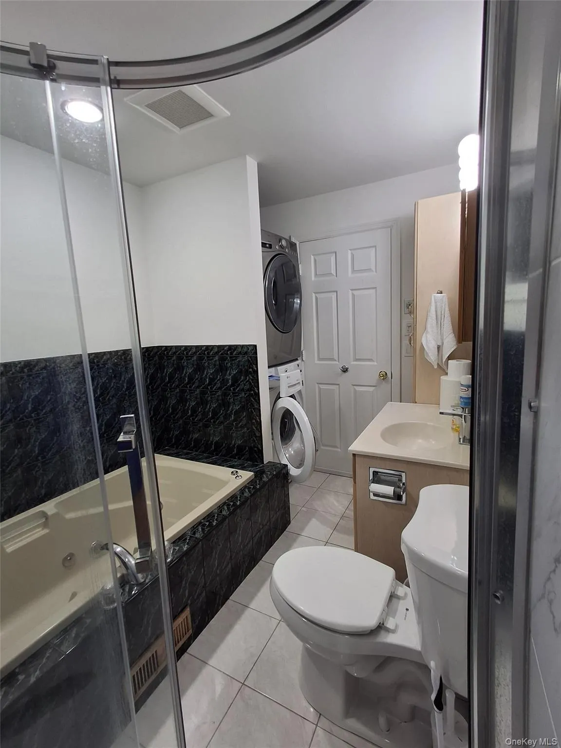 Full bathroom featuring light tile patterned floors, vanity, and stacked washer and clothes dryer Full bathroom featuring light tile patterned floors, vanity, and stacked washer and clothes dryer