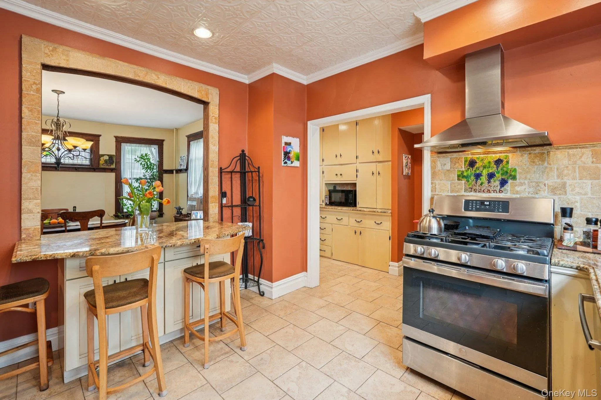 Kitchen featuring stainless steel gas stove, wall chimney range hood, crown molding, light stone countertops, and an ornate ceiling Kitchen featuring stainless steel gas stove, wall chimney range hood, crown molding, light stone countertops, and an ornate ceiling