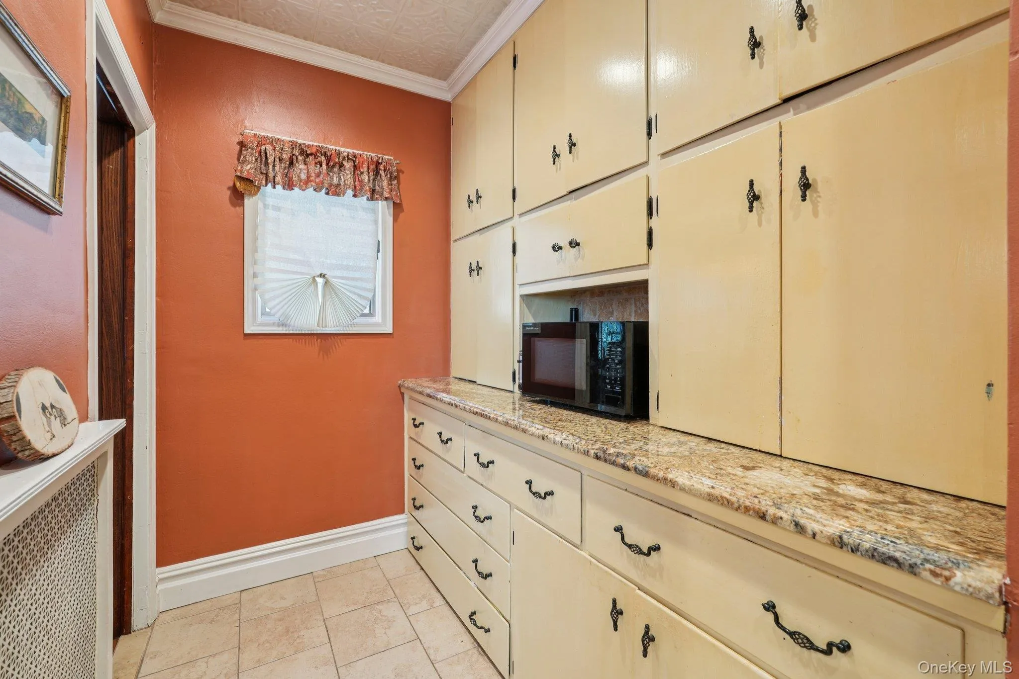 Kitchen featuring cream cabinetry, an ornate ceiling, ornamental molding, radiator heating unit, and black microwave Kitchen featuring cream cabinetry, an ornate ceiling, ornamental molding, radiator heating unit, and black microwave