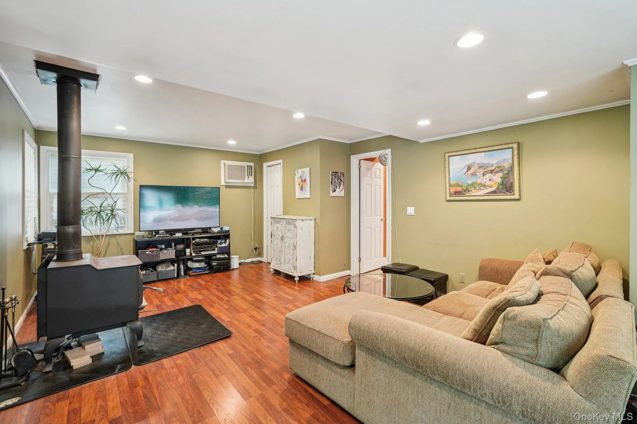 Living area with a wood stove, recessed lighting, ornamental molding, wood finished floors, and a wall mounted air conditioner Living area with a wood stove, recessed lighting, ornamental molding, wood finished floors, and a wall mounted air conditioner