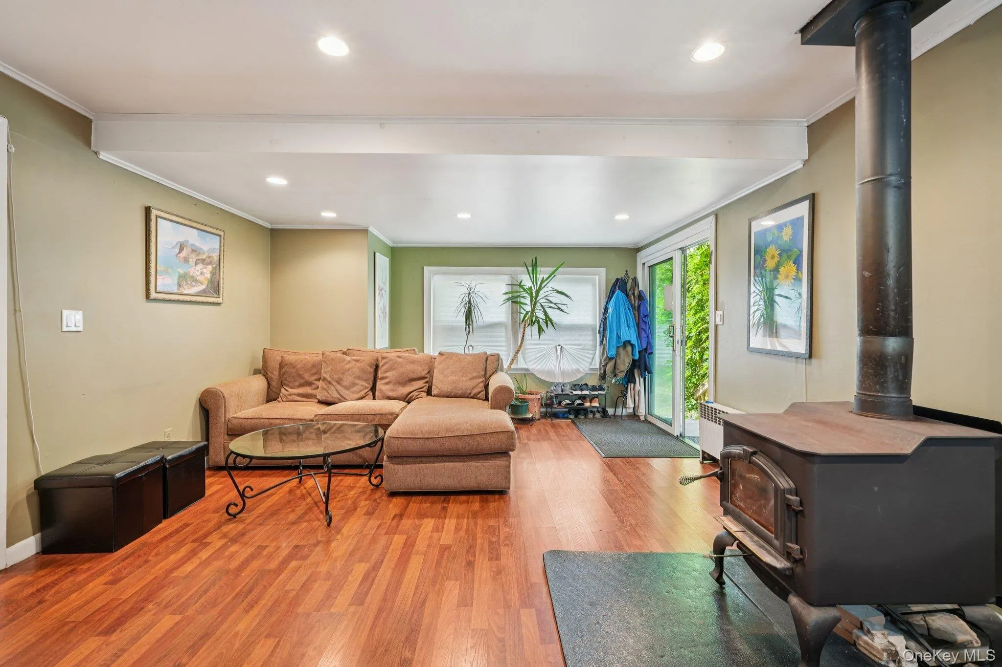 Living room featuring a wood stove, wood finished floors, crown molding, recessed lighting, and radiator heating unit Living room featuring a wood stove, wood finished floors, crown molding, recessed lighting, and radiator heating unit