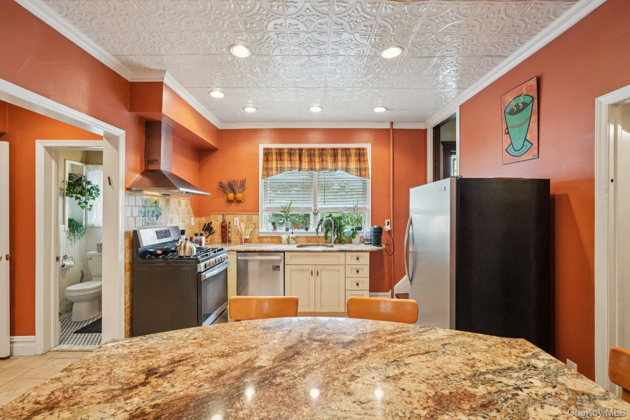 Kitchen featuring ornamental molding, appliances with stainless steel finishes, wall chimney range hood, light stone countertops, and backsplash Kitchen featuring ornamental molding, appliances with stainless steel finishes, wall chimney range hood, light stone countertops, and backsplash