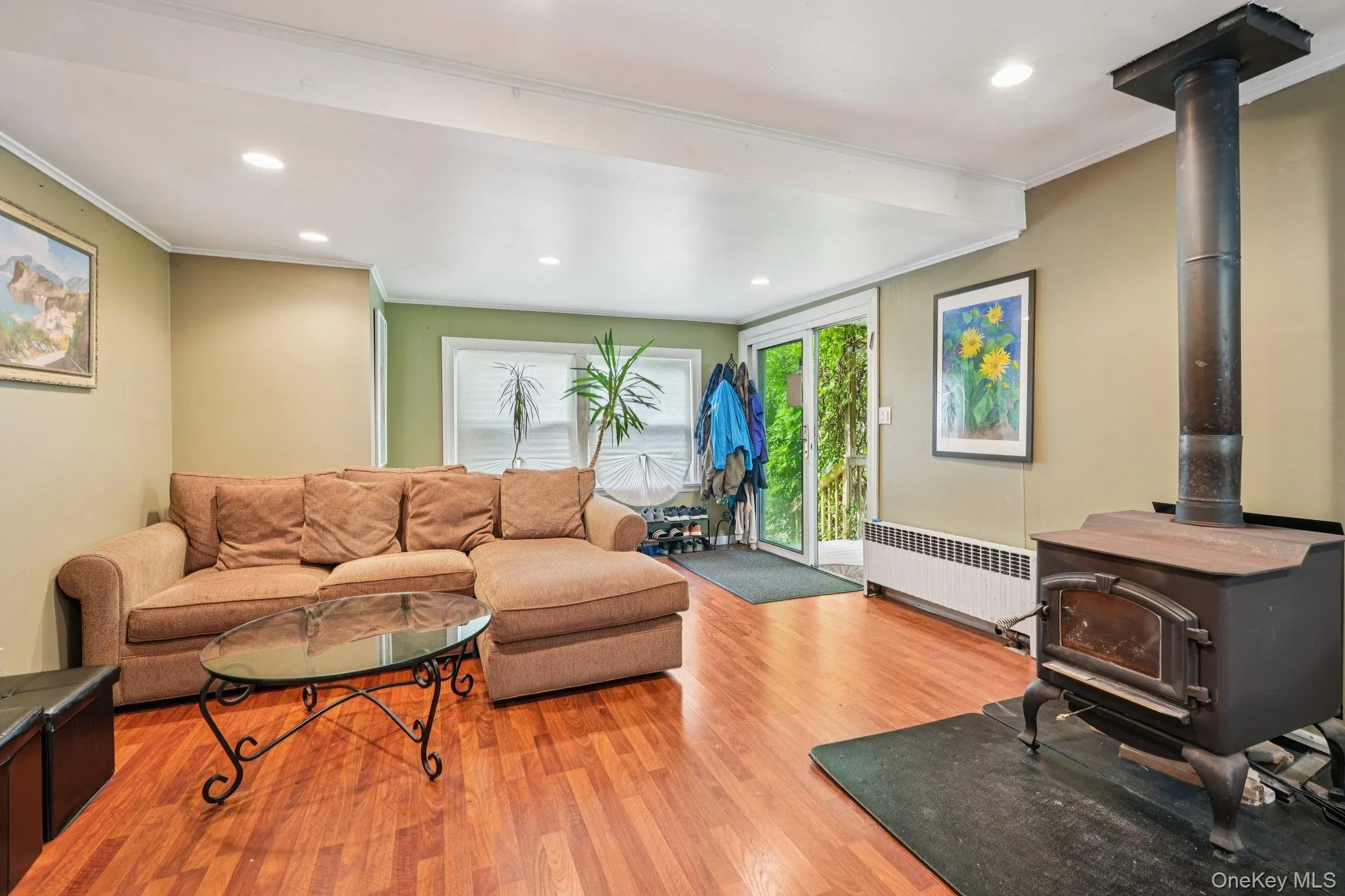Living room with a wood stove, ornamental molding, recessed lighting, wood finished floors, and radiator Living room with a wood stove, ornamental molding, recessed lighting, wood finished floors, and radiator