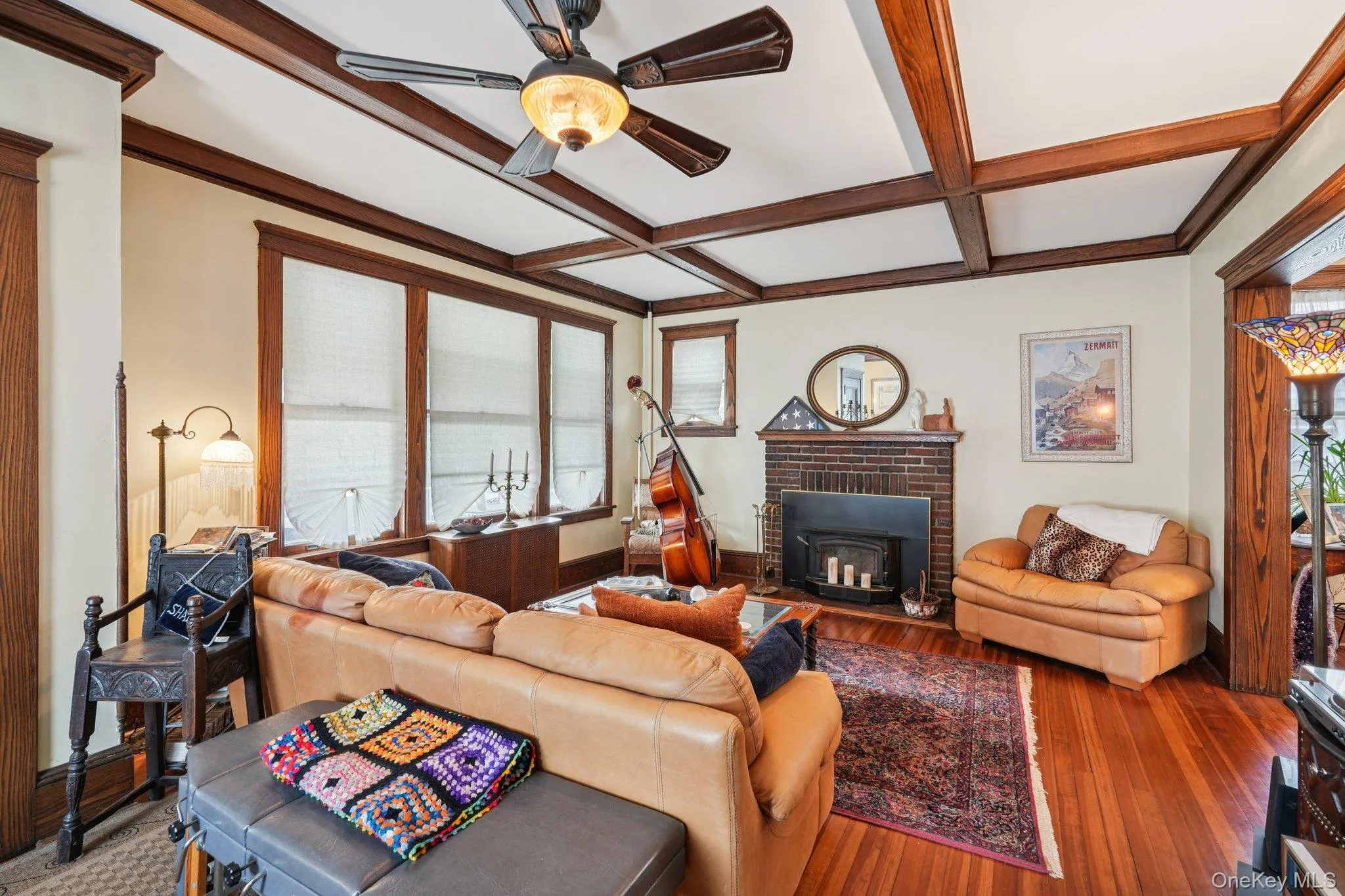 Living room featuring coffered ceiling, beam ceiling, wood finished floors, a ceiling fan, and a wood stove Living room featuring coffered ceiling, beam ceiling, wood finished floors, a ceiling fan, and a wood stove
