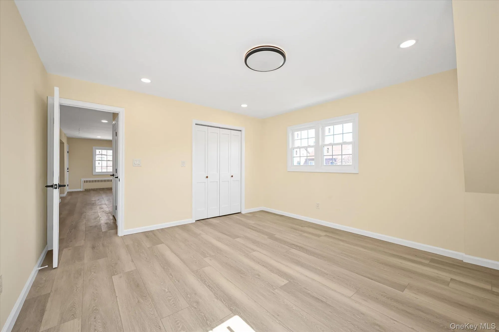 Unfurnished bedroom with recessed lighting, light wood finished floors, radiator, and a closet Unfurnished bedroom with recessed lighting, light wood finished floors, radiator, and a closet
