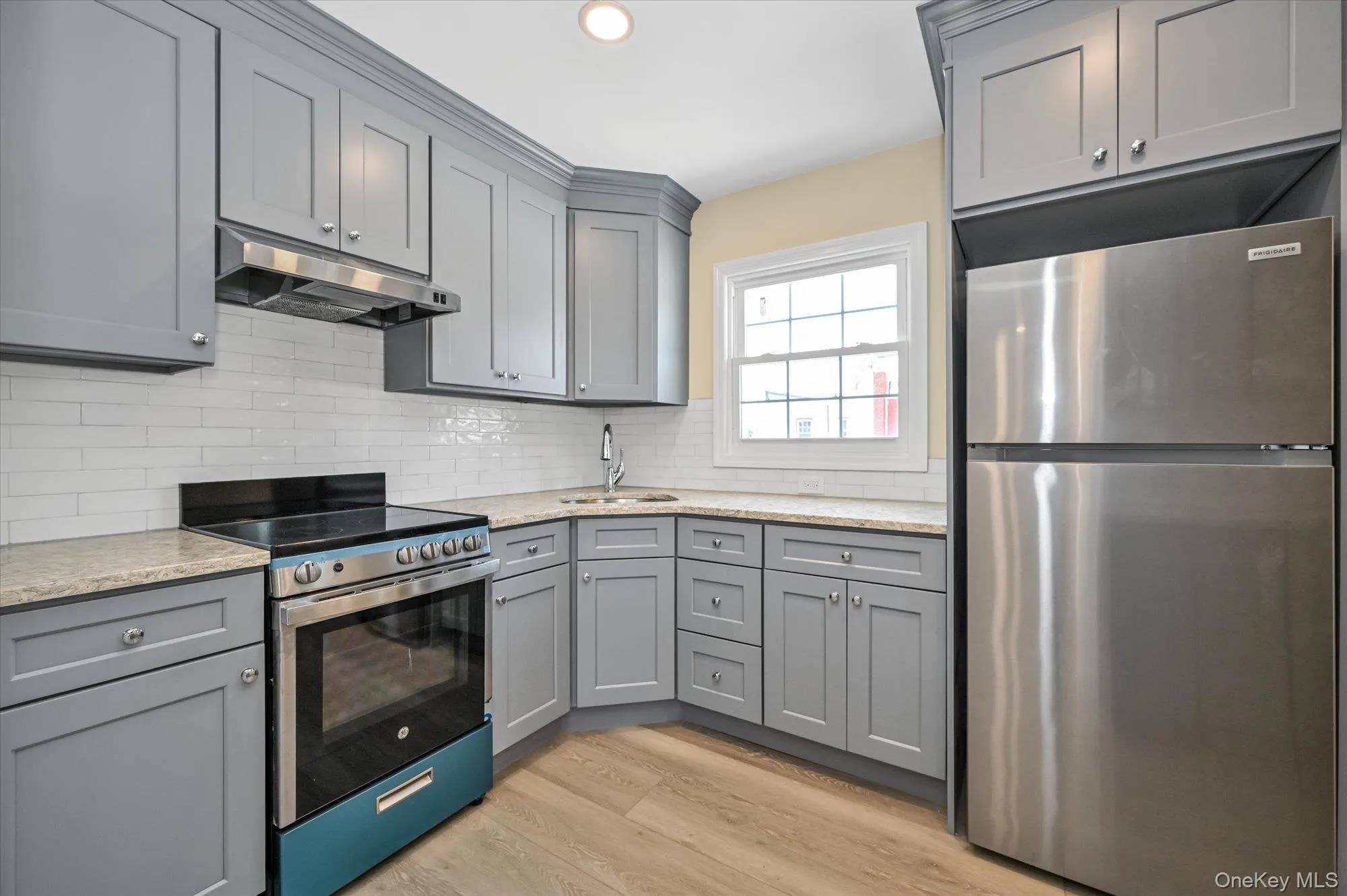 Kitchen featuring gray cabinetry, appliances with stainless steel finishes, under cabinet range hood, light wood-style flooring, and backsplash Kitchen featuring gray cabinetry, appliances with stainless steel finishes, under cabinet range hood, light wood-style flooring, and backsplash