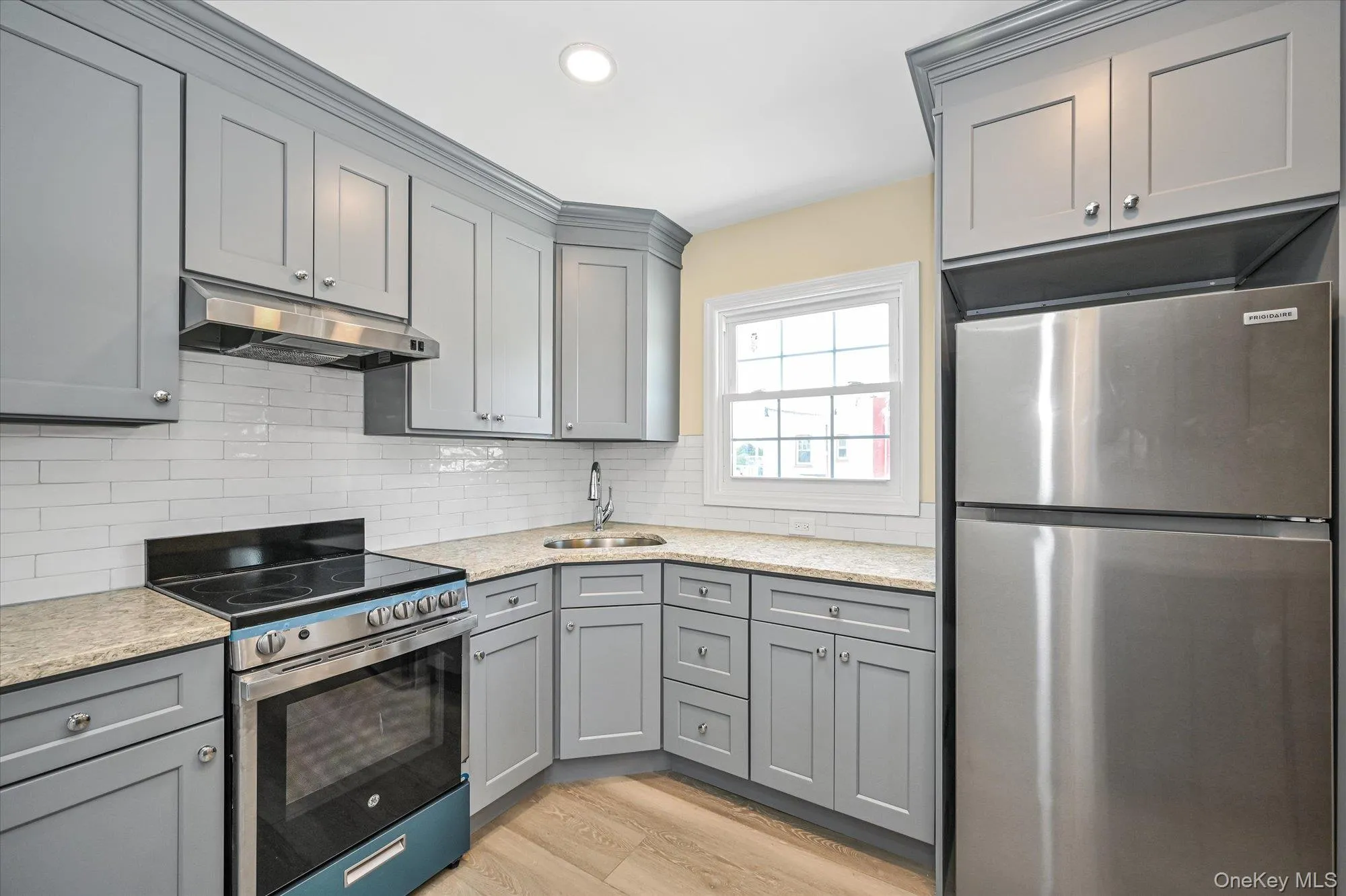 Kitchen with gray cabinetry, appliances with stainless steel finishes, under cabinet range hood, light wood-style flooring, and backsplash Kitchen with gray cabinetry, appliances with stainless steel finishes, under cabinet range hood, light wood-style flooring, and backsplash