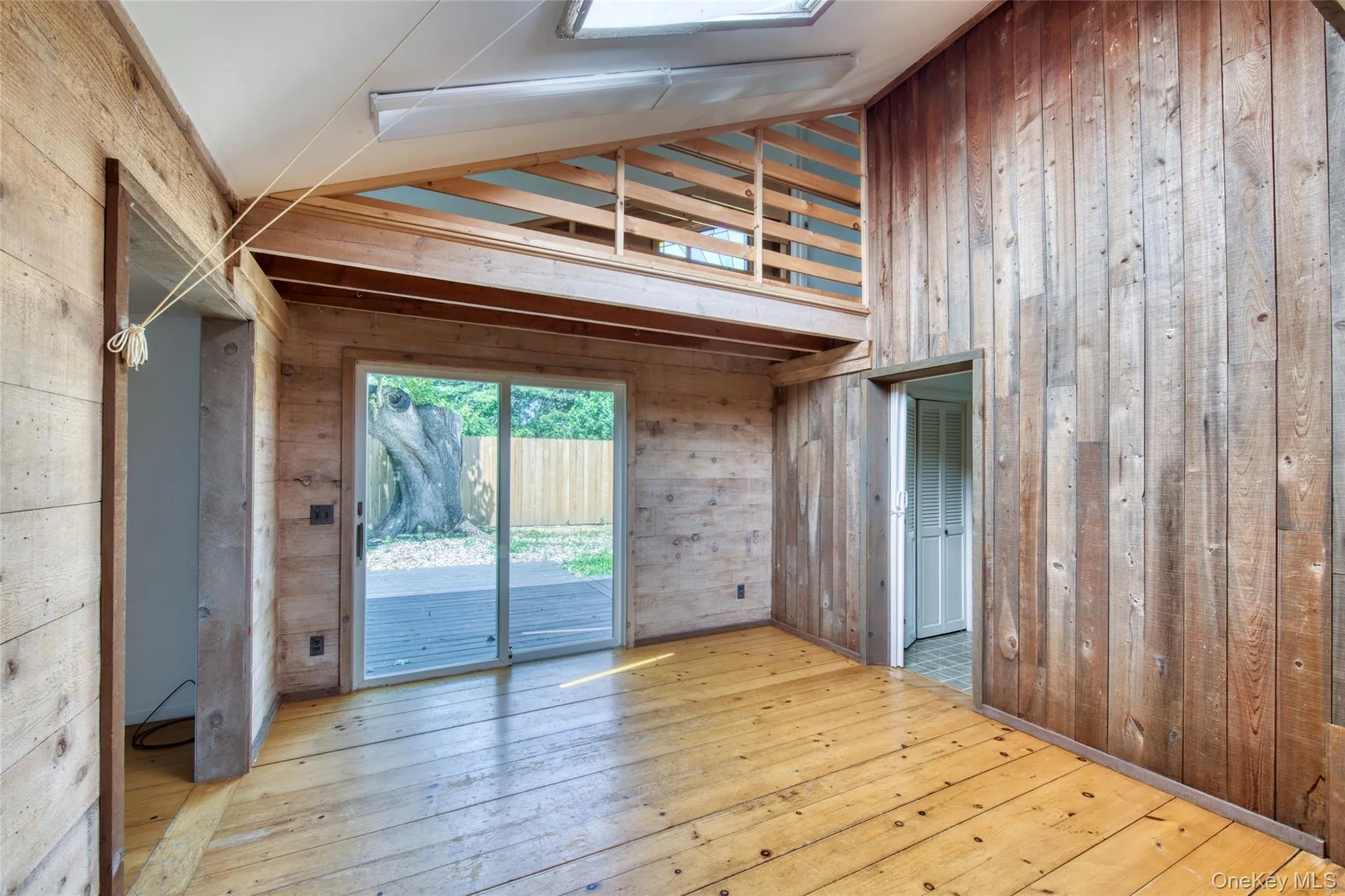 Unfurnished living room with high vaulted ceiling, wood walls, hardwood / wood-style flooring, and a skylight Unfurnished living room with high vaulted ceiling, wood walls, hardwood / wood-style flooring, and a skylight