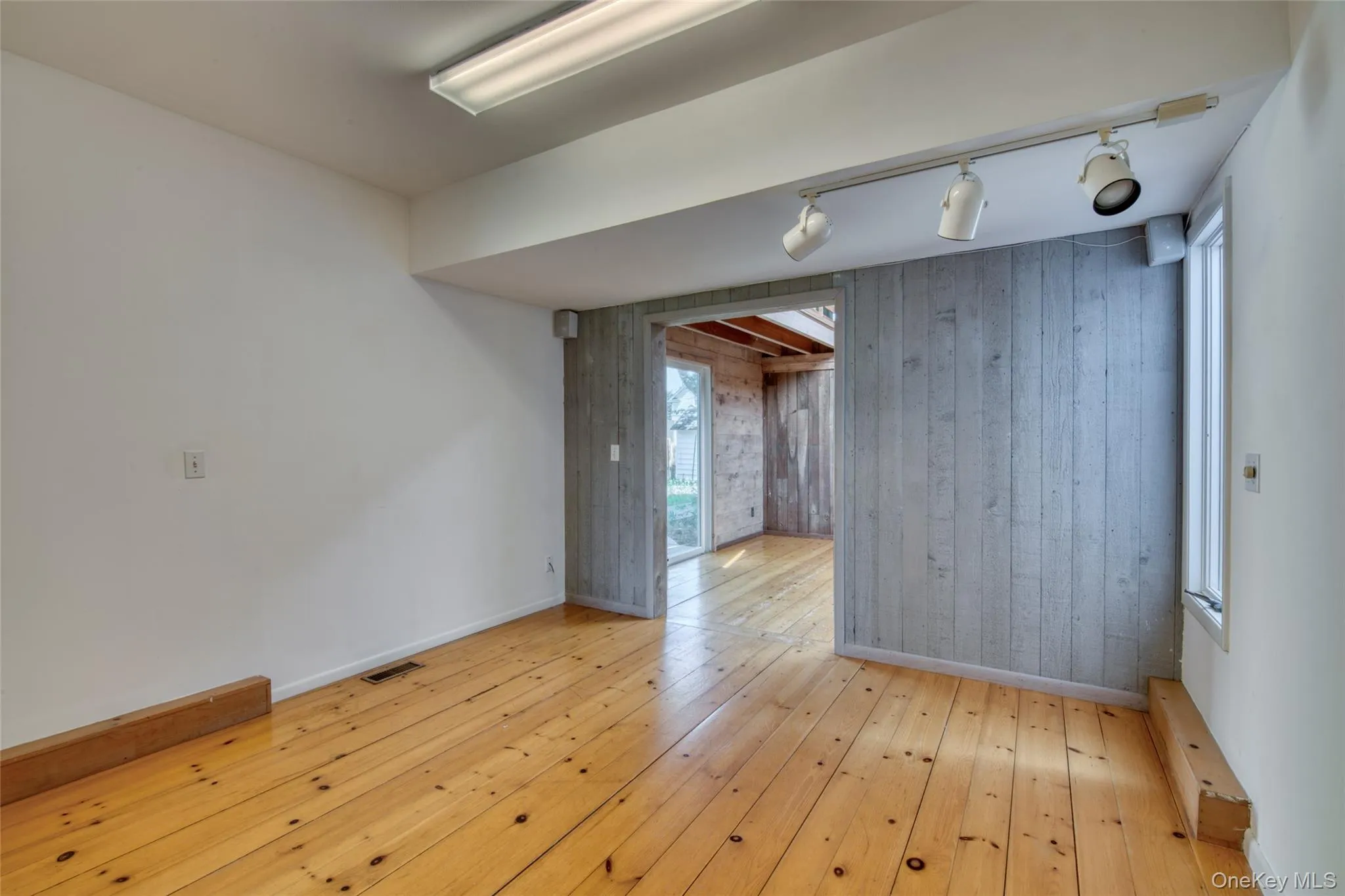 Spare room featuring wooden walls, light wood-type flooring, and rail lighting Spare room featuring wooden walls, light wood-type flooring, and rail lighting