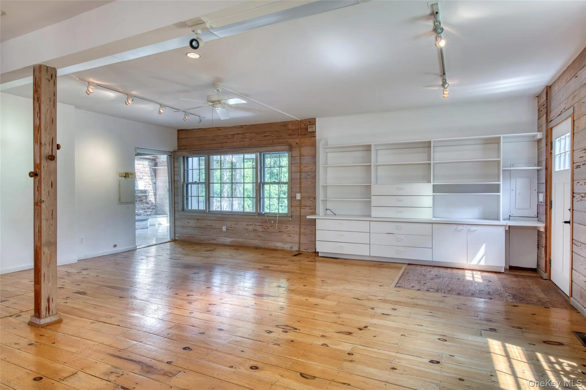 Unfurnished living room featuring track lighting, light wood finished floors, wood walls, and a ceiling fan Unfurnished living room featuring track lighting, light wood finished floors, wood walls, and a ceiling fan