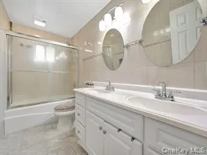 Full bathroom featuring combined bath / shower with glass door, double vanity, and tile walls Full bathroom featuring combined bath / shower with glass door, double vanity, and tile walls