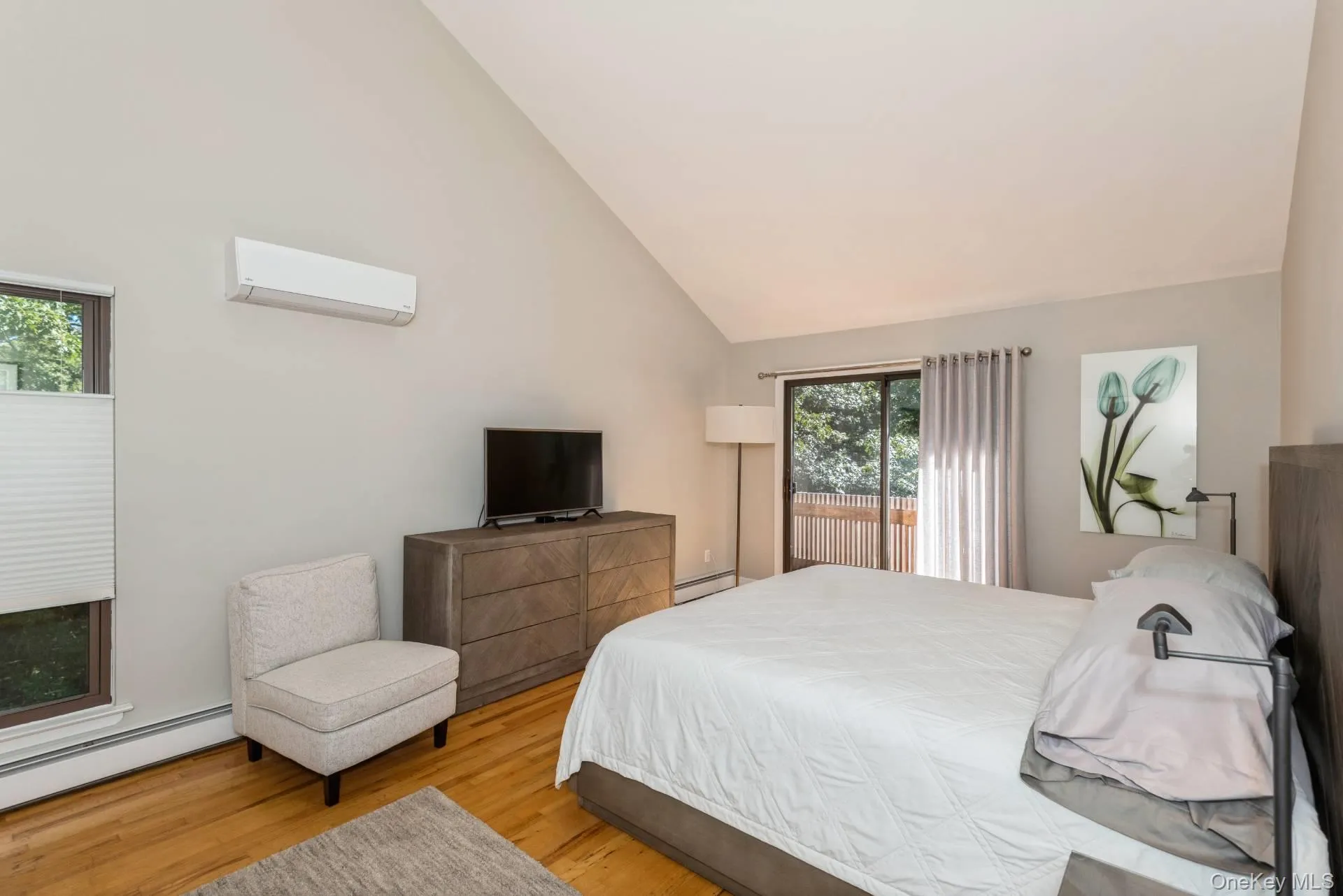 Bedroom featuring an AC wall unit, light wood finished floors, access to outside, high vaulted ceiling, and a baseboard heating unit Bedroom featuring an AC wall unit, light wood finished floors, access to outside, high vaulted ceiling, and a baseboard heating unit
