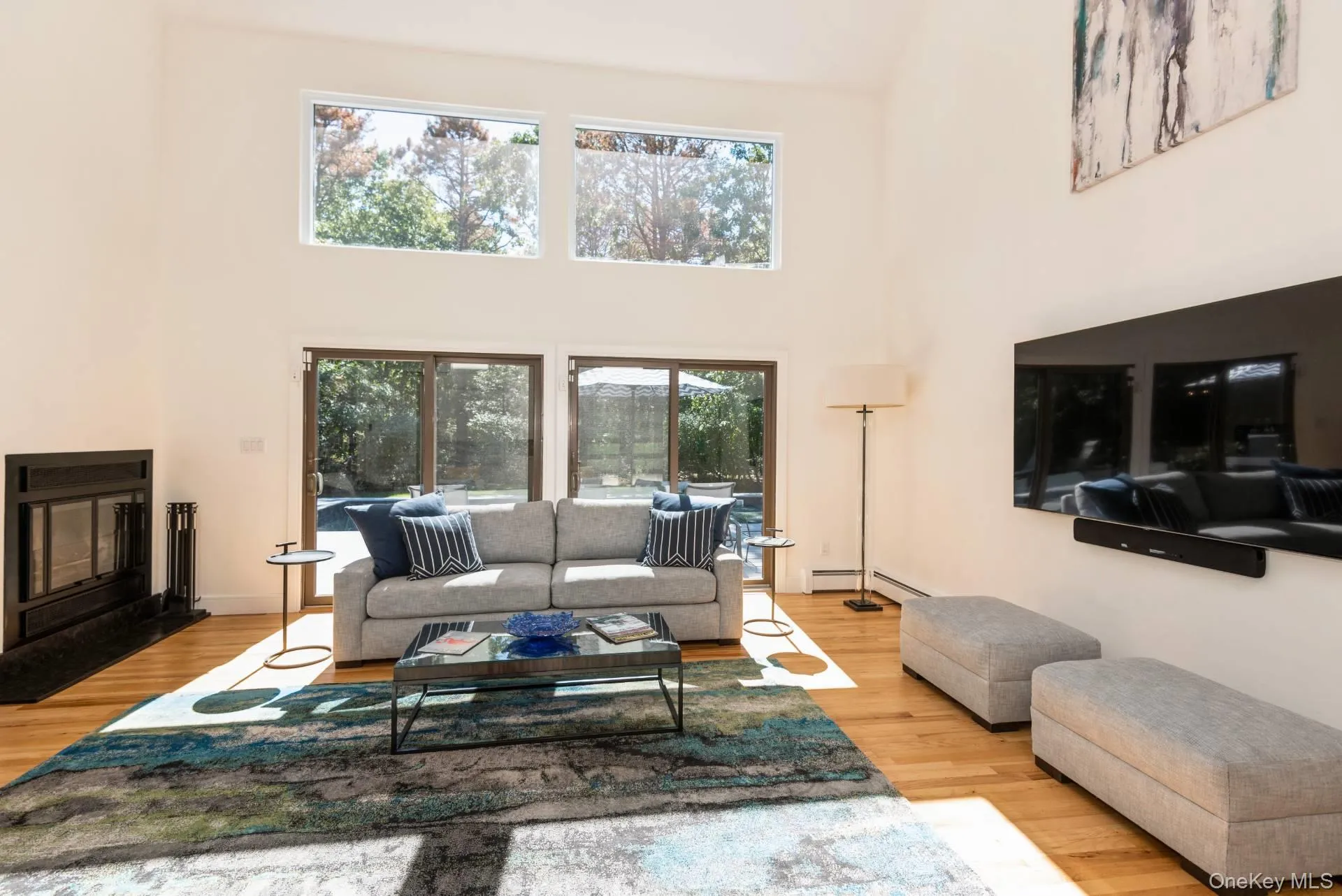 Living room featuring a high ceiling, a glass covered fireplace, and light wood-style flooring Living room featuring a high ceiling, a glass covered fireplace, and light wood-style flooring
