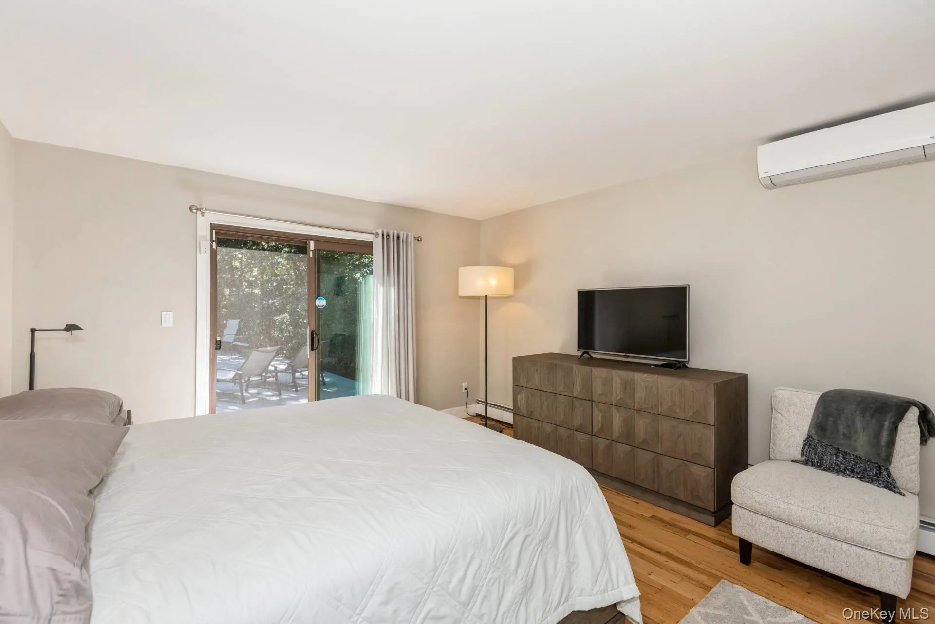 Bedroom featuring light wood-type flooring, access to exterior, a wall mounted air conditioner, and baseboard heating Bedroom featuring light wood-type flooring, access to exterior, a wall mounted air conditioner, and baseboard heating