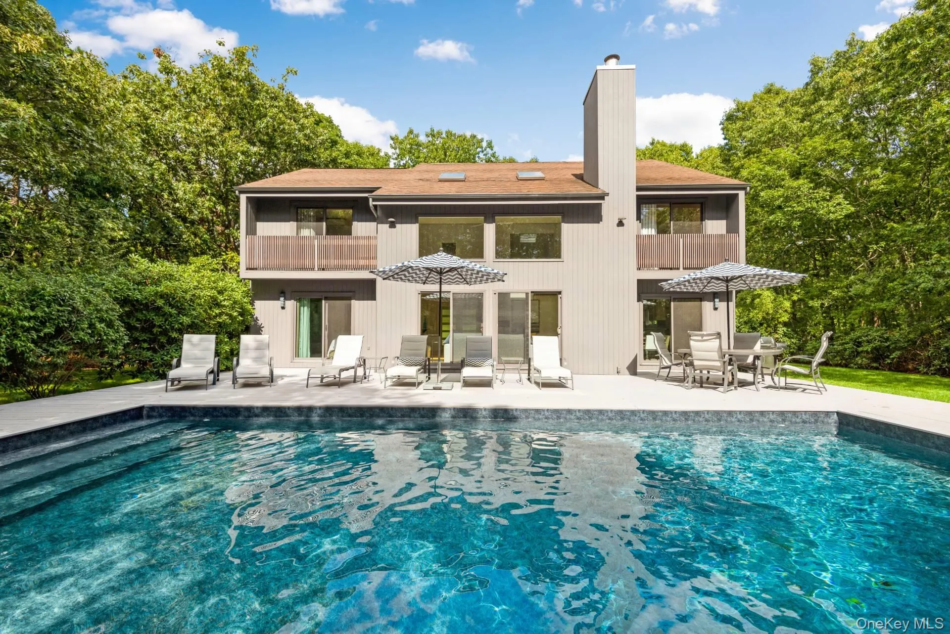 Back of property featuring a balcony, a patio, an outdoor pool, and a chimney Back of property featuring a balcony, a patio, an outdoor pool, and a chimney