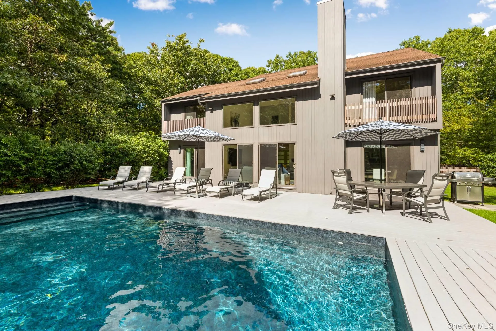 Back of property with an outdoor pool, outdoor dining space, a patio area, and a wooden deck Back of property with an outdoor pool, outdoor dining space, a patio area, and a wooden deck