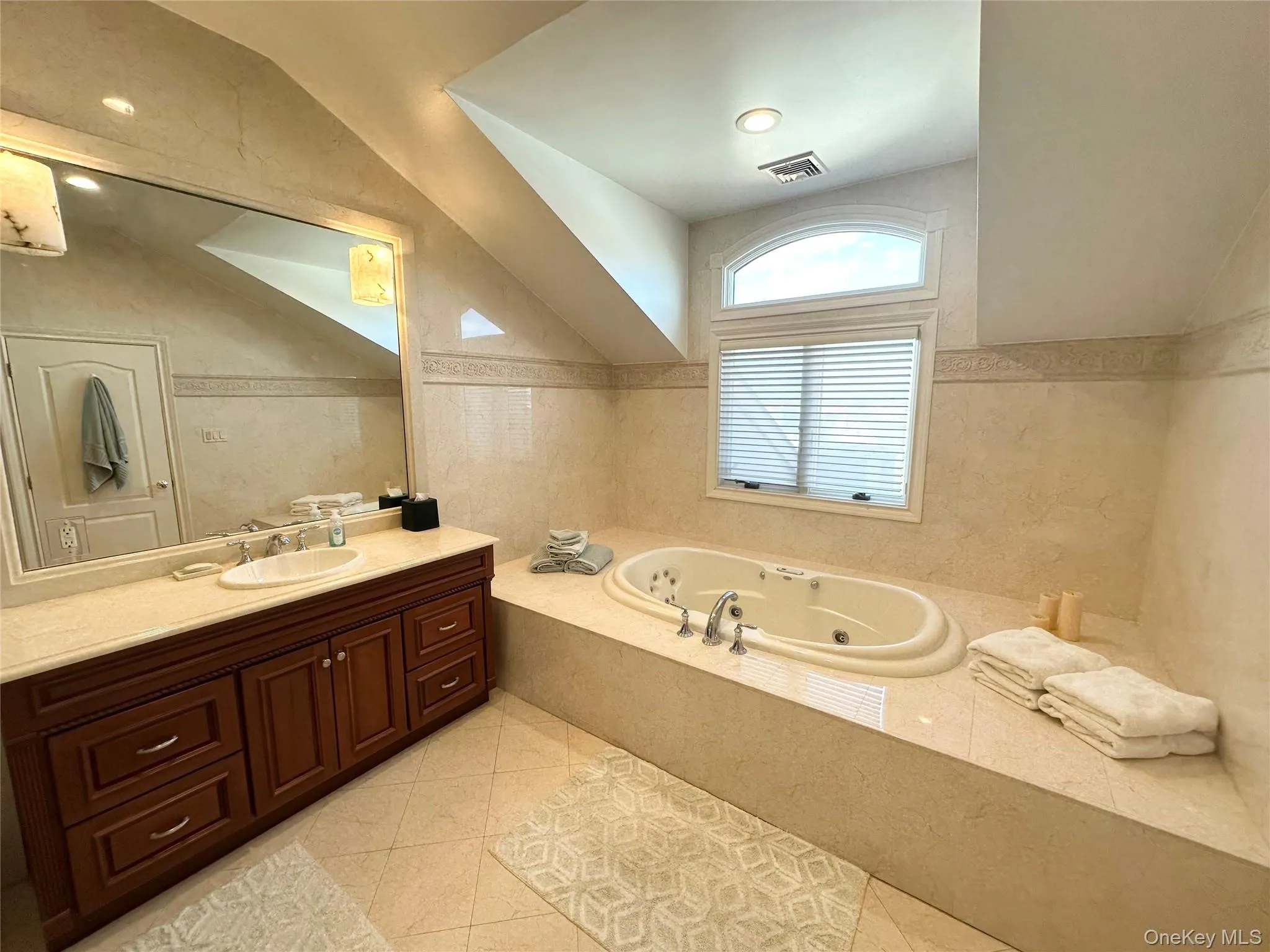 Bathroom with lofted ceiling, vanity, a tub with jets, light tile patterned floors, and tile walls Bathroom with lofted ceiling, vanity, a tub with jets, light tile patterned floors, and tile walls