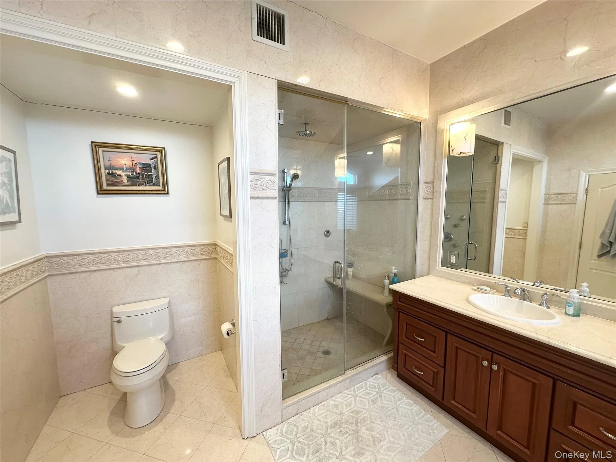 Bathroom featuring vanity, a shower stall, tile walls, light tile patterned floors, and wainscoting Bathroom featuring vanity, a shower stall, tile walls, light tile patterned floors, and wainscoting