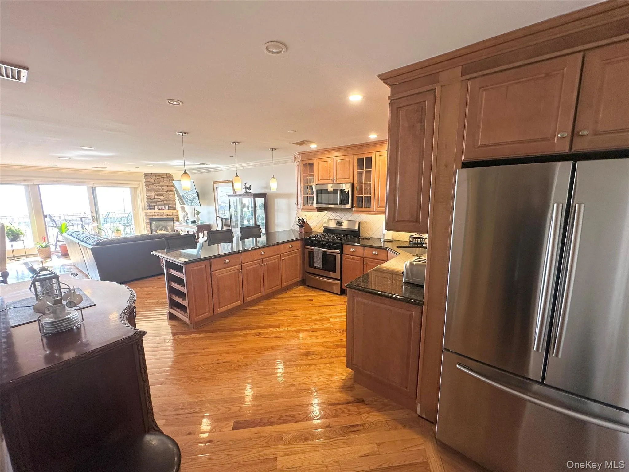 Kitchen with appliances with stainless steel finishes, glass insert cabinets, a peninsula, brown cabinetry, and hanging light fixtures Kitchen with appliances with stainless steel finishes, glass insert cabinets, a peninsula, brown cabinetry, and hanging light fixtures