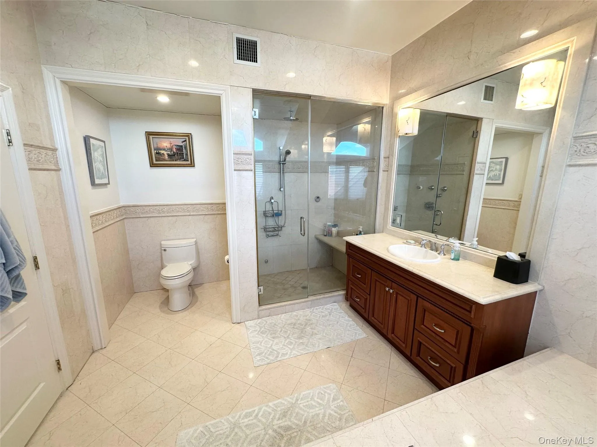 Bathroom featuring tile walls, vanity, a stall shower, wainscoting, and light tile patterned floors Bathroom featuring tile walls, vanity, a stall shower, wainscoting, and light tile patterned floors