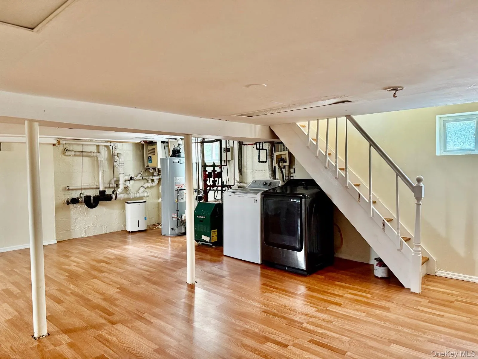 Below grade area with light wood-type flooring, washing machine and clothes dryer, gas water heater, and a heating unit Below grade area with light wood-type flooring, washing machine and clothes dryer, gas water heater, and a heating unit