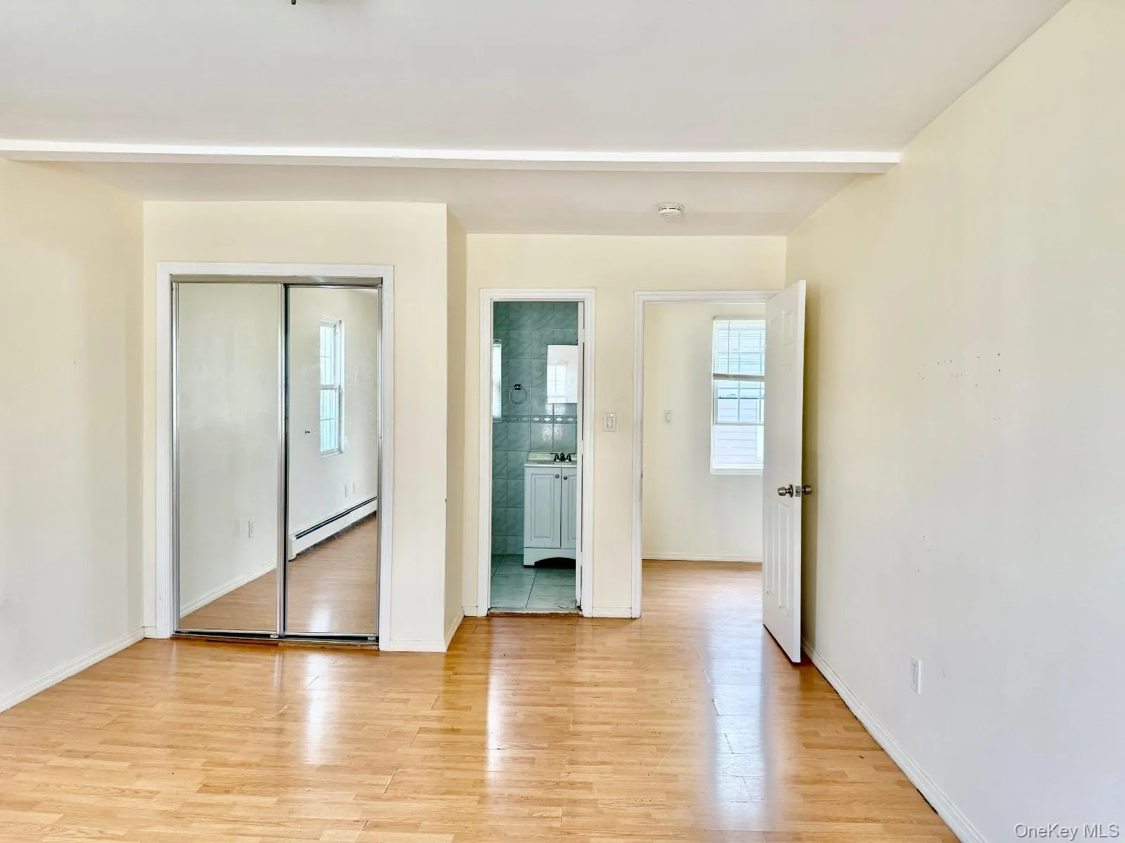 Unfurnished bedroom with a closet, light wood-type flooring, baseboard heating, and connected bathroom Unfurnished bedroom with a closet, light wood-type flooring, baseboard heating, and connected bathroom
