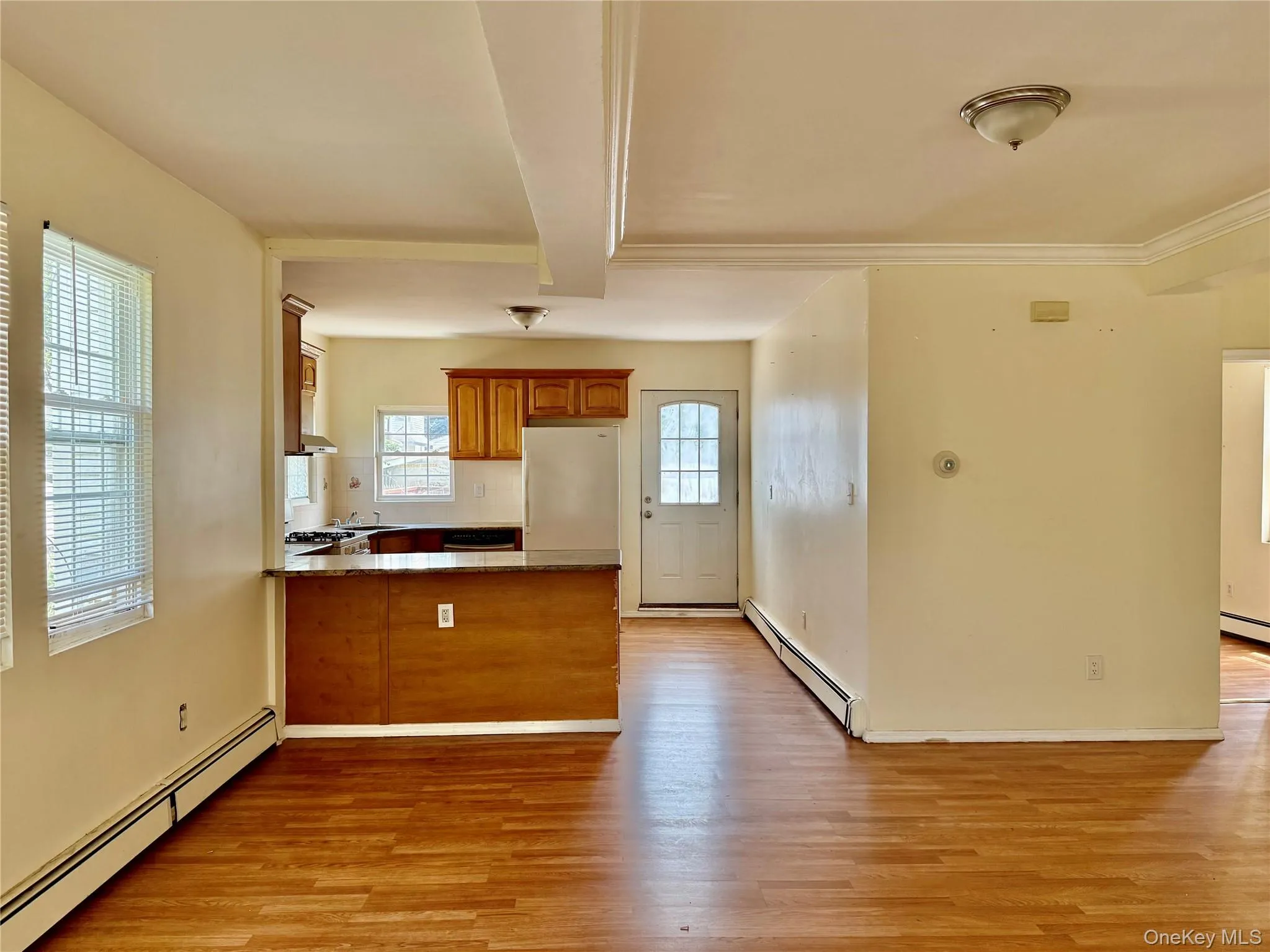 Kitchen with a baseboard radiator, a peninsula, light wood-style floors, brown cabinets, and beam ceiling Kitchen with a baseboard radiator, a peninsula, light wood-style floors, brown cabinets, and beam ceiling