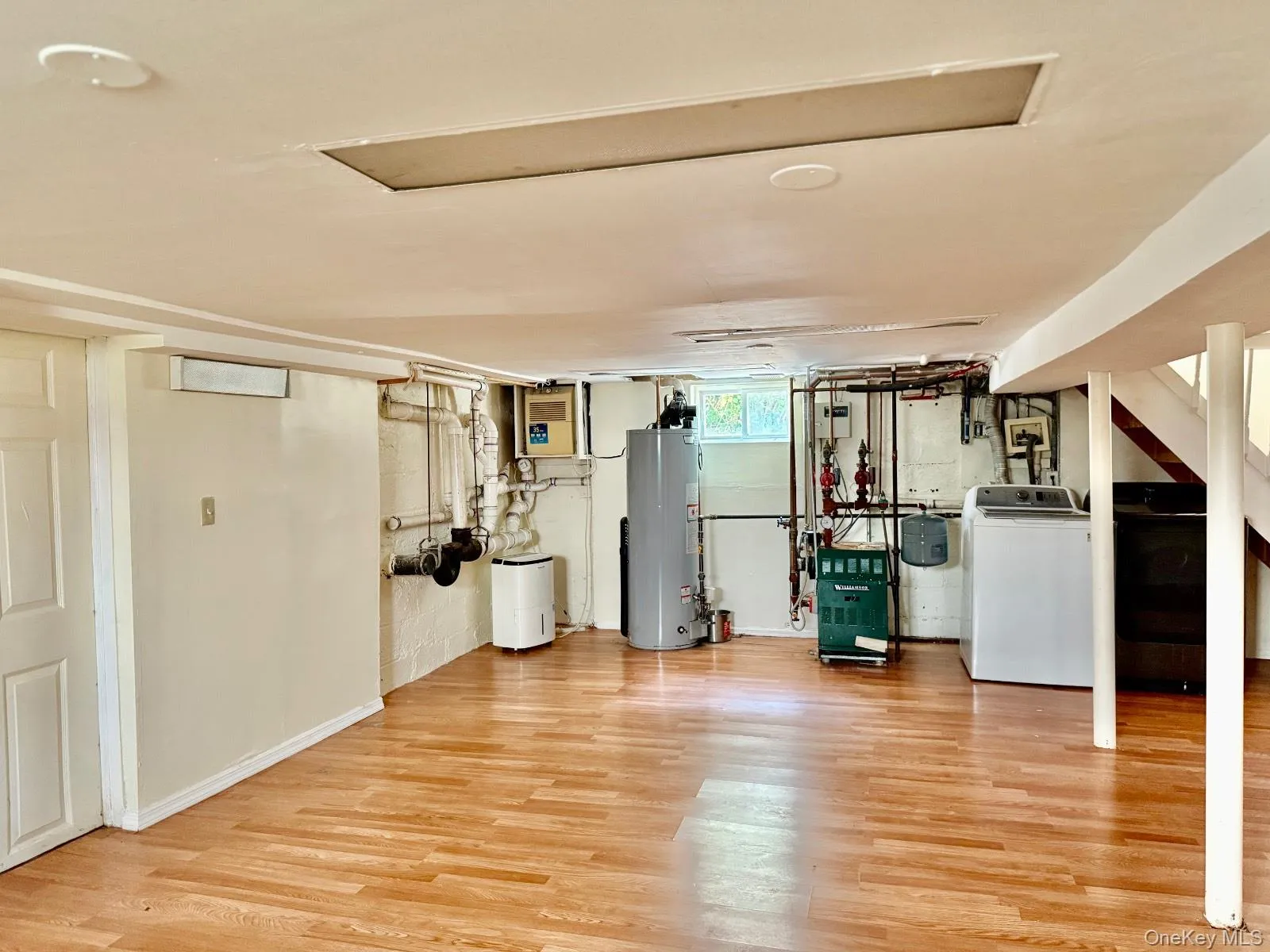 Below grade area featuring light wood-style flooring, water heater, washer / dryer, and a heating unit Below grade area featuring light wood-style flooring, water heater, washer / dryer, and a heating unit