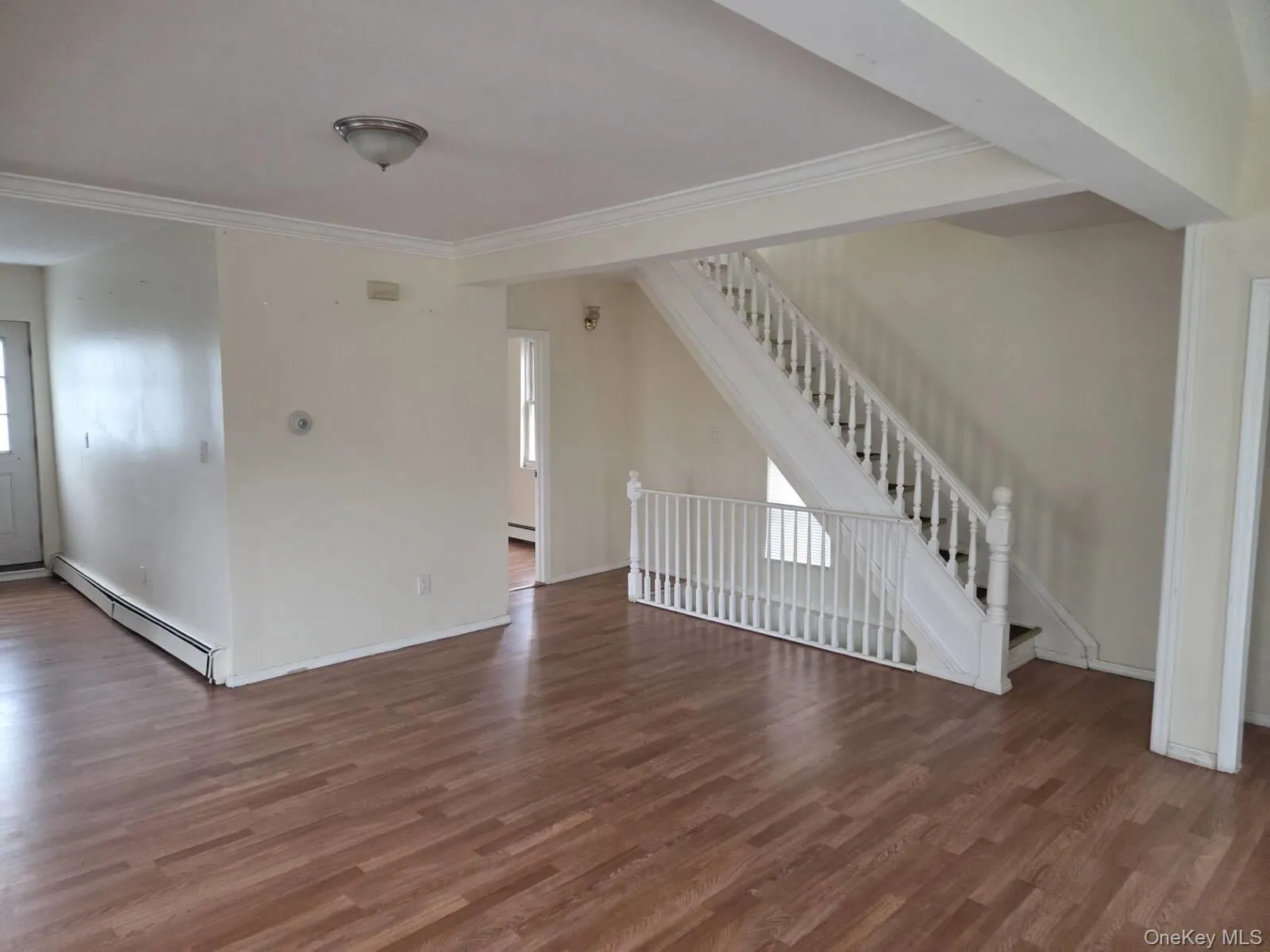 Unfurnished living room with dark wood-style flooring, a baseboard heating unit, stairs, and crown molding Unfurnished living room with dark wood-style flooring, a baseboard heating unit, stairs, and crown molding