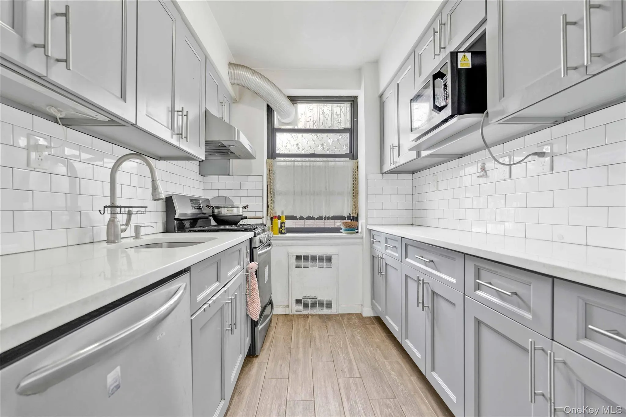 Kitchen with appliances with stainless steel finishes, gray cabinets, light stone counters, under cabinet range hood, and light wood-type flooring Kitchen with appliances with stainless steel finishes, gray cabinets, light stone counters, under cabinet range hood, and light wood-type flooring