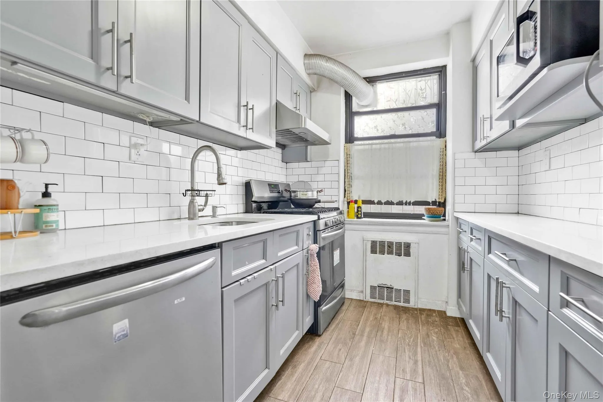 Kitchen with gray cabinets, appliances with stainless steel finishes, under cabinet range hood, light stone countertops, and tasteful backsplash Kitchen with gray cabinets, appliances with stainless steel finishes, under cabinet range hood, light stone countertops, and tasteful backsplash