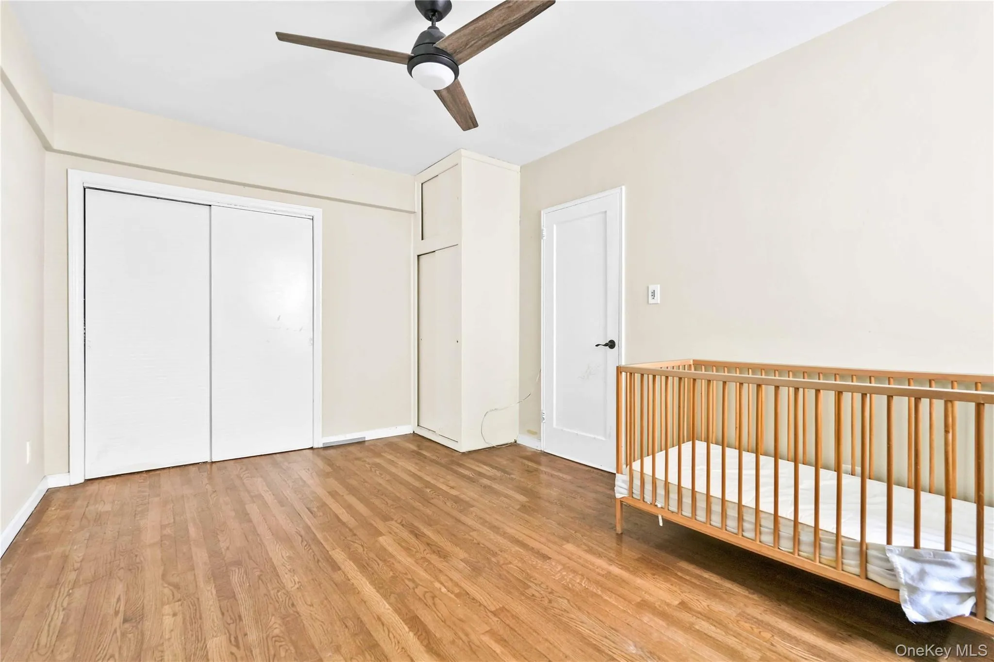 Unfurnished bedroom with light wood-type flooring, a crib, ceiling fan, and a closet Unfurnished bedroom with light wood-type flooring, a crib, ceiling fan, and a closet