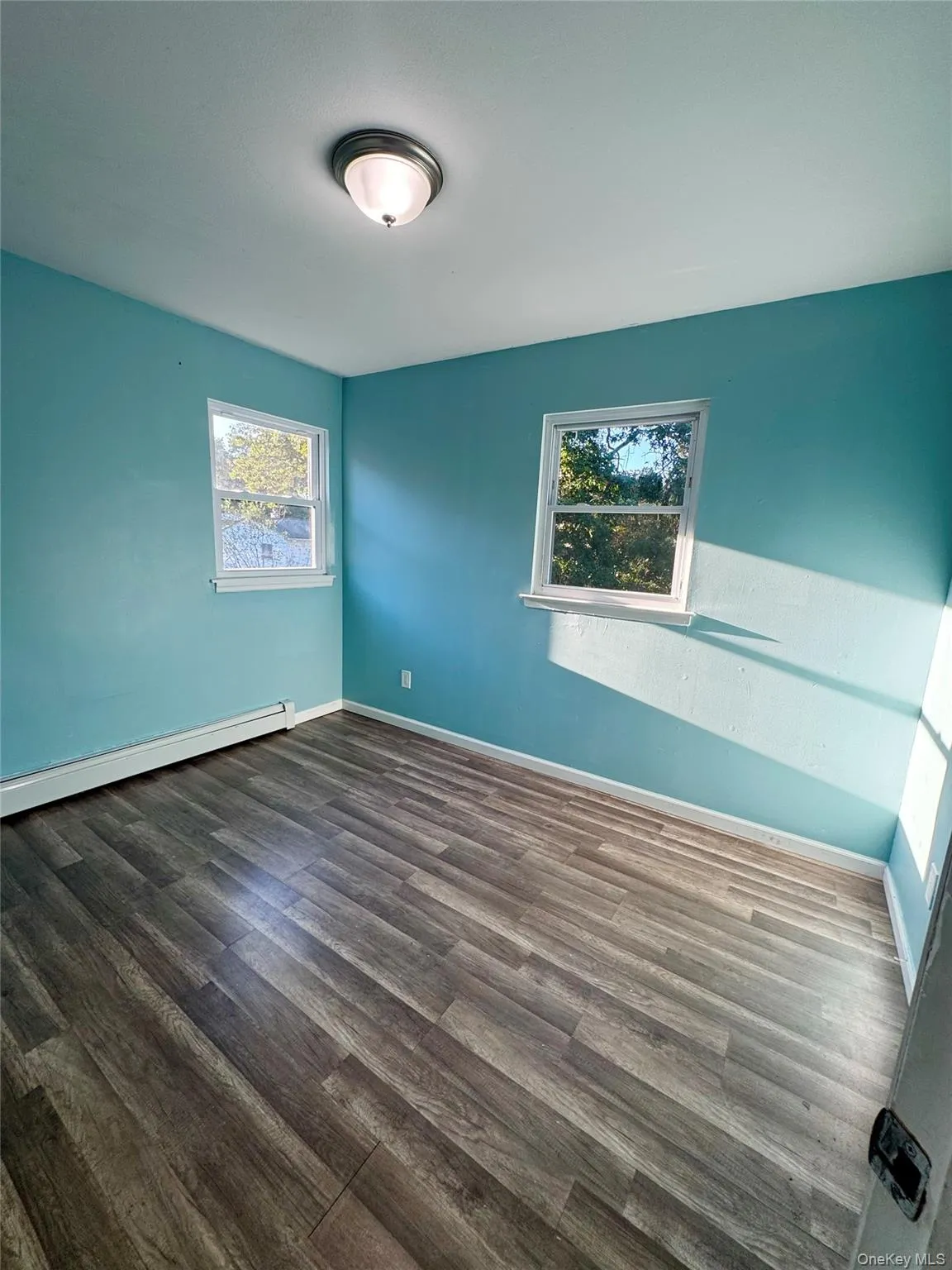 Spare room featuring baseboard heating and dark wood-type flooring Spare room featuring baseboard heating and dark wood-type flooring