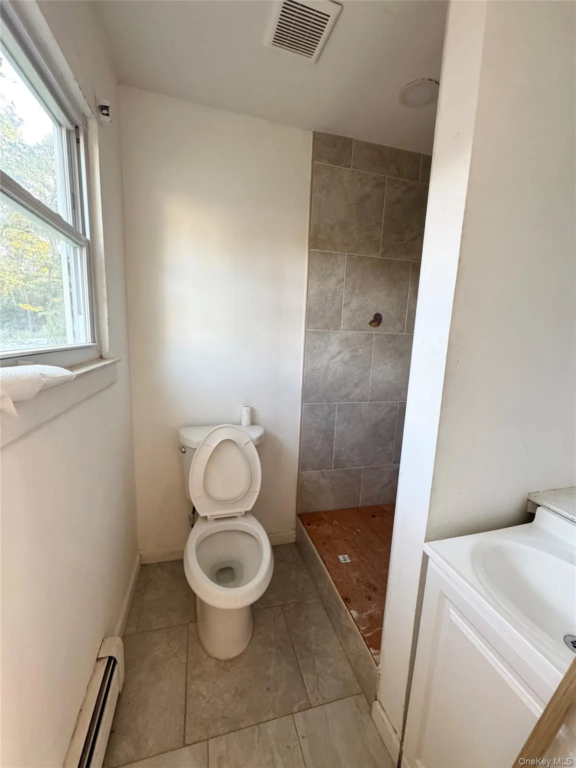 Bathroom featuring vanity, a shower stall, baseboard heating, and light tile patterned flooring Bathroom featuring vanity, a shower stall, baseboard heating, and light tile patterned flooring