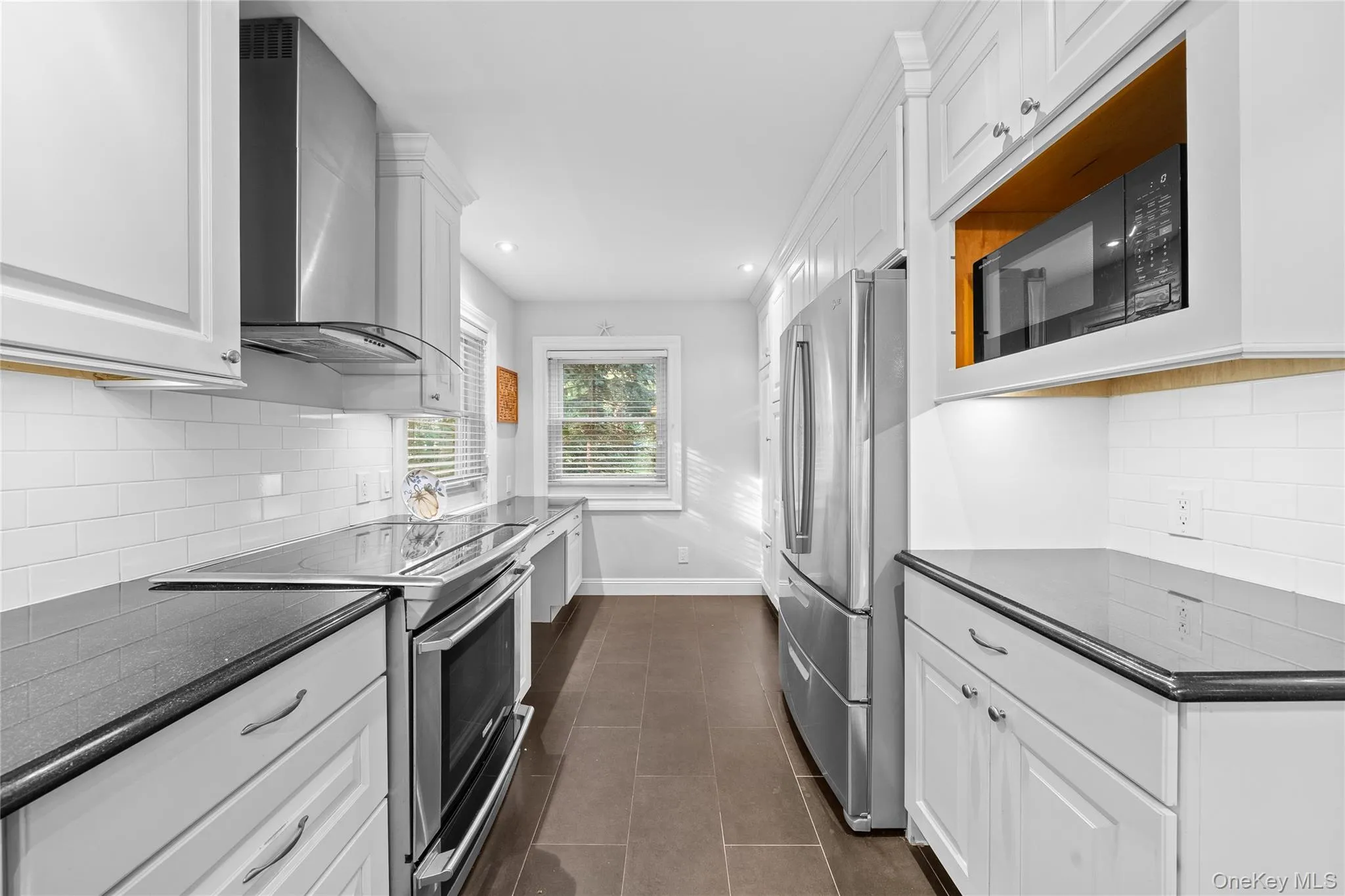 Kitchen with tasteful backsplash, white cabinetry, stainless steel appliances, wall chimney range hood, and recessed lighting Kitchen with tasteful backsplash, white cabinetry, stainless steel appliances, wall chimney range hood, and recessed lighting