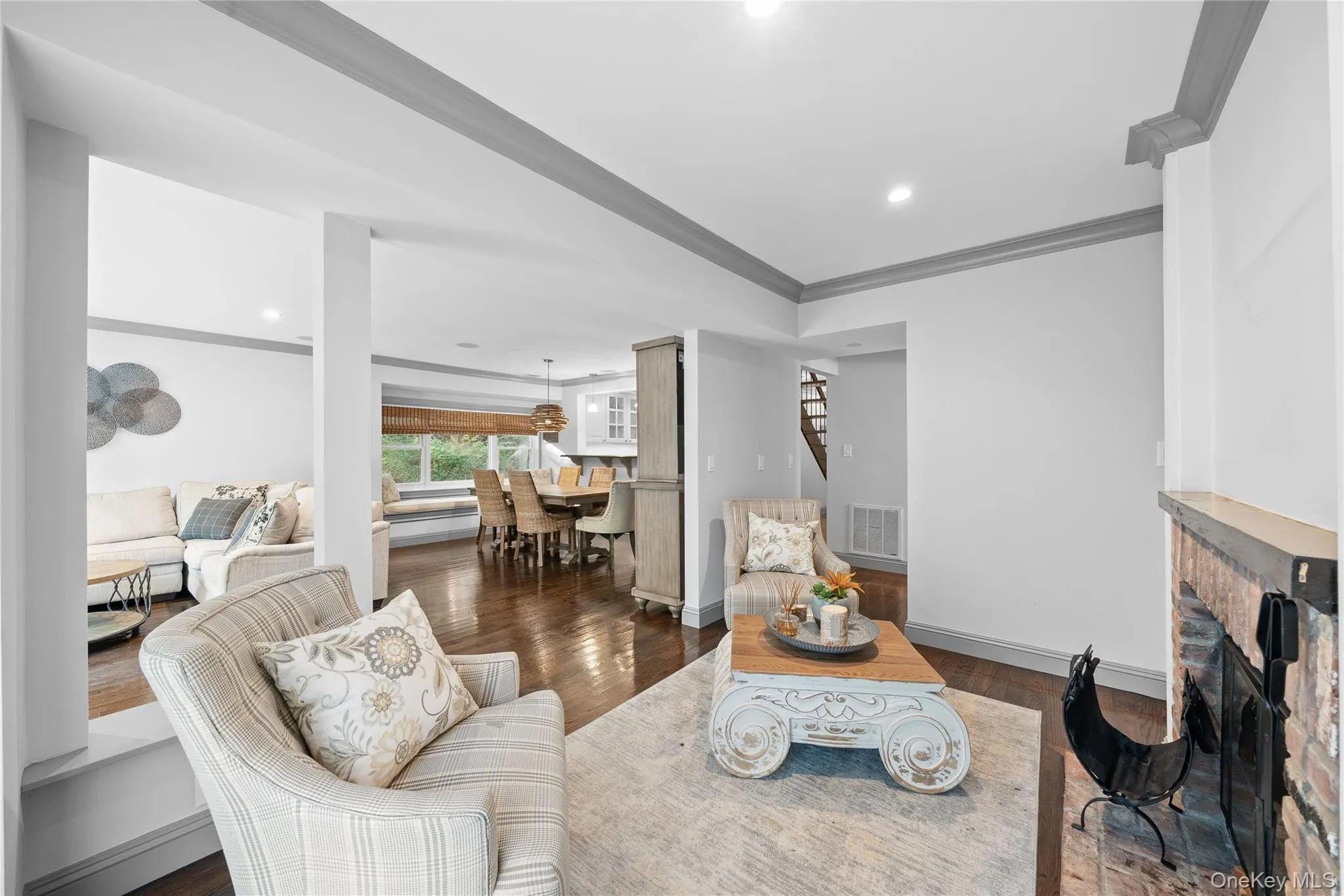 Living room featuring crown molding, dark wood-style flooring, a brick fireplace, recessed lighting, and stairway Living room featuring crown molding, dark wood-style flooring, a brick fireplace, recessed lighting, and stairway