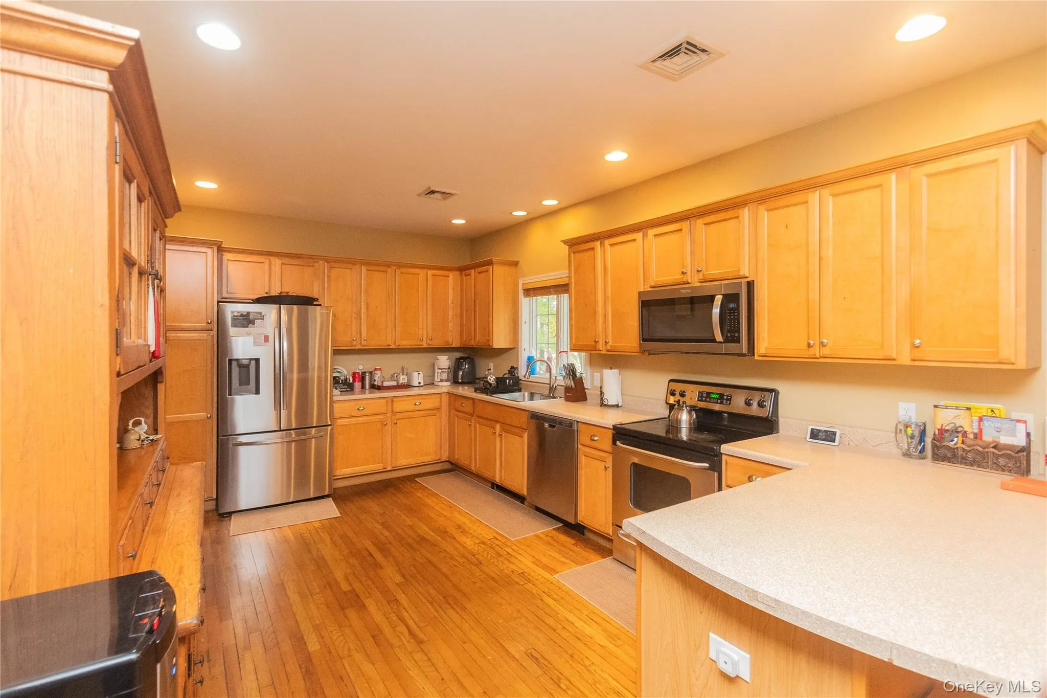 Kitchen with appliances with stainless steel finishes, light brown cabinets, recessed lighting, light wood-type flooring, and a peninsula Kitchen with appliances with stainless steel finishes, light brown cabinets, recessed lighting, light wood-type flooring, and a peninsula