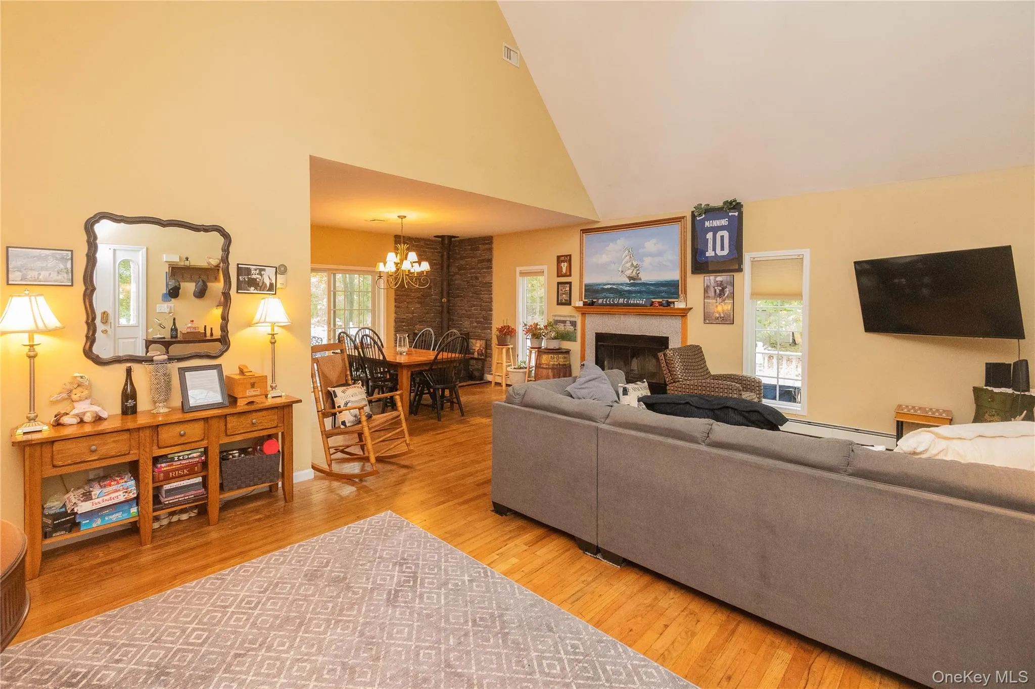 Living room with healthy amount of natural light, light wood-style floors, a fireplace, high vaulted ceiling, and a chandelier Living room with healthy amount of natural light, light wood-style floors, a fireplace, high vaulted ceiling, and a chandelier
