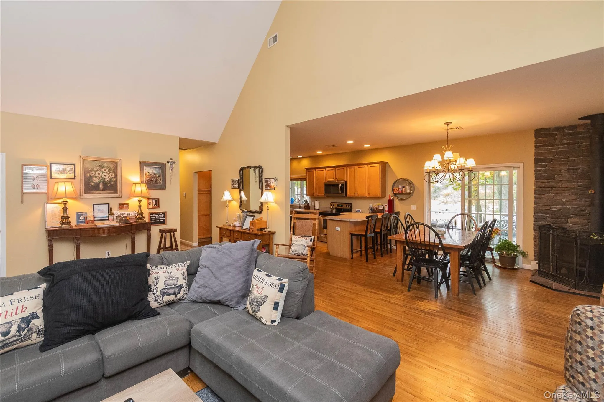 Living area featuring high vaulted ceiling, a wood stove, light wood finished floors, a chandelier, and recessed lighting Living area featuring high vaulted ceiling, a wood stove, light wood finished floors, a chandelier, and recessed lighting