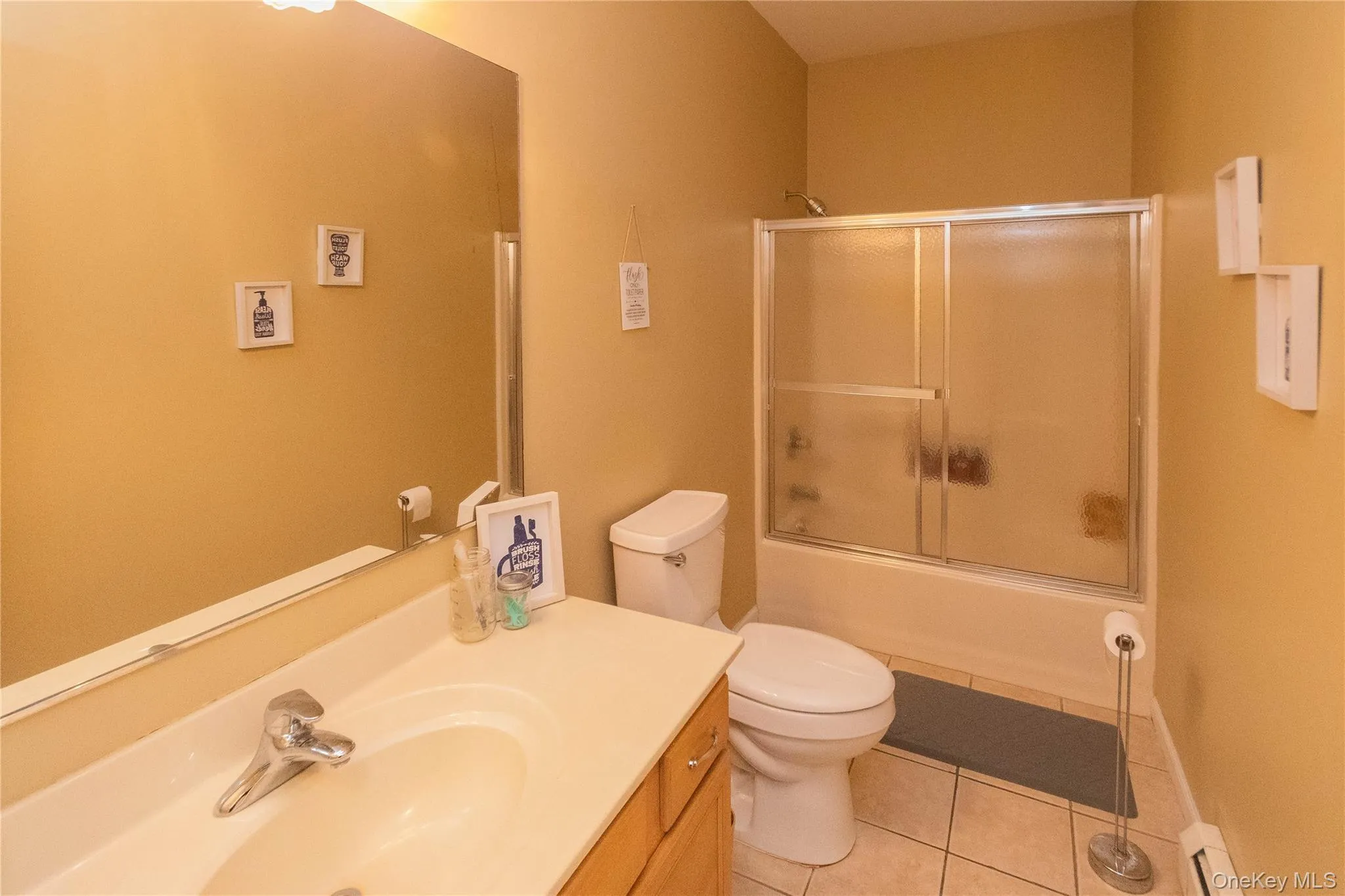 Bathroom featuring light tile patterned floors, vanity, combined bath / shower with glass door, and baseboard heating Bathroom featuring light tile patterned floors, vanity, combined bath / shower with glass door, and baseboard heating