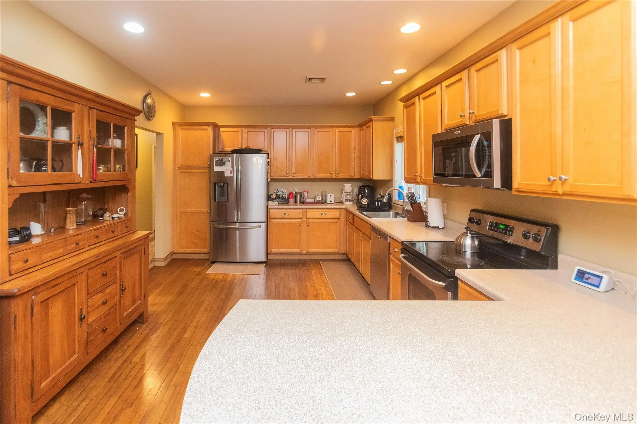 Kitchen featuring stainless steel appliances, glass insert cabinets, light countertops, recessed lighting, and light wood-type flooring Kitchen featuring stainless steel appliances, glass insert cabinets, light countertops, recessed lighting, and light wood-type flooring