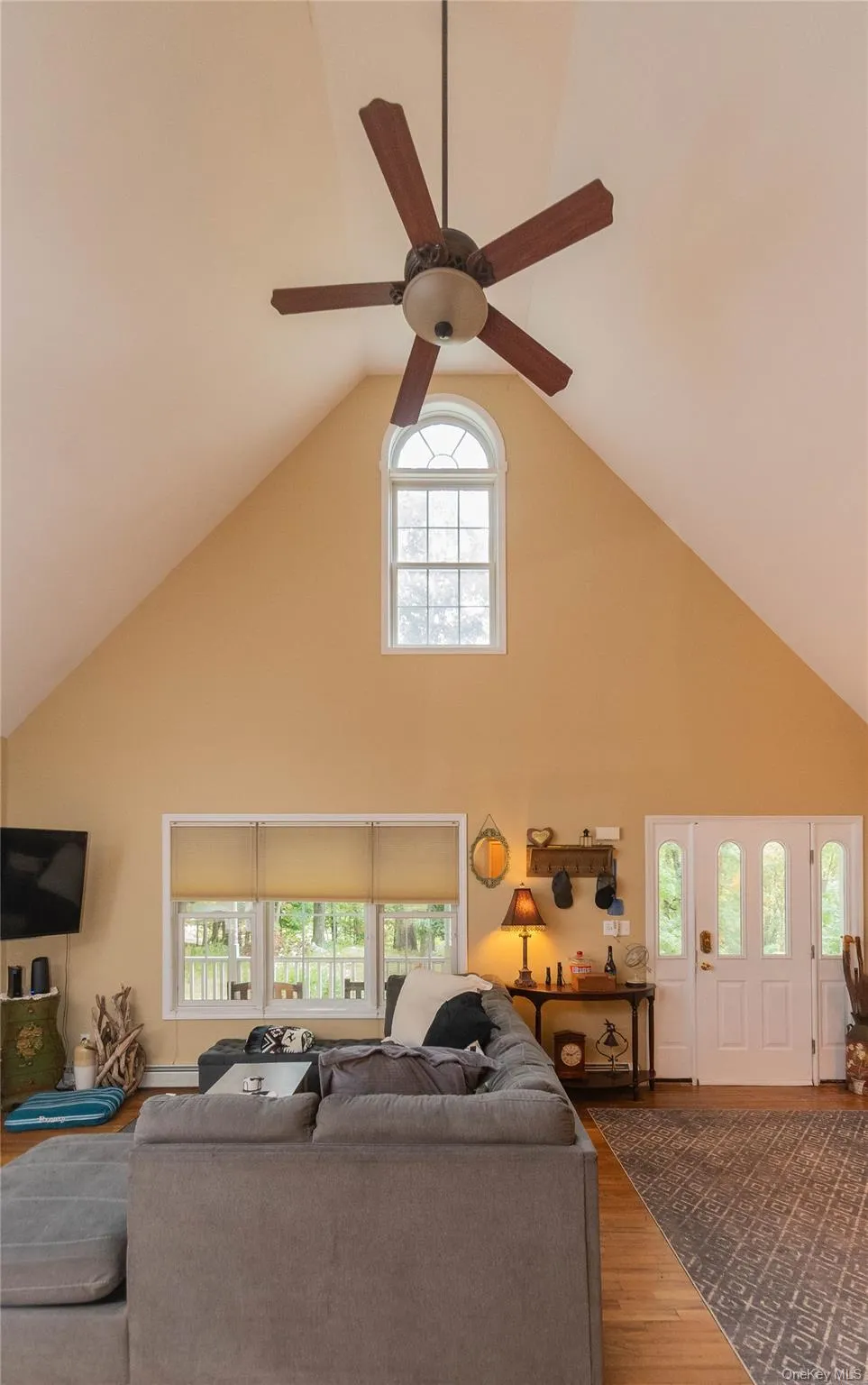 Living room with high vaulted ceiling, wood finished floors, plenty of natural light, and ceiling fan Living room with high vaulted ceiling, wood finished floors, plenty of natural light, and ceiling fan