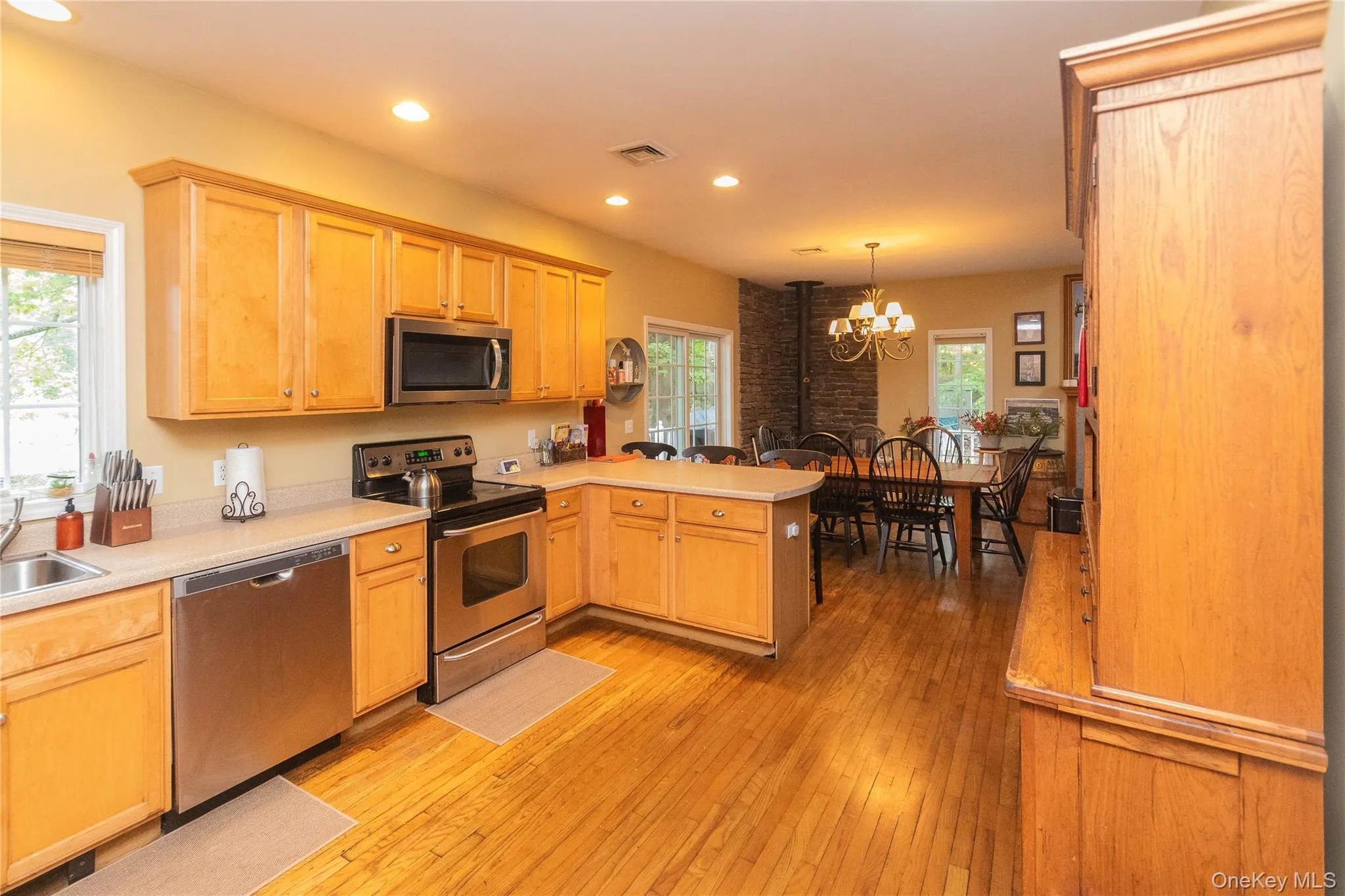 Kitchen featuring a peninsula, stainless steel appliances, light wood-style floors, light countertops, and a chandelier Kitchen featuring a peninsula, stainless steel appliances, light wood-style floors, light countertops, and a chandelier