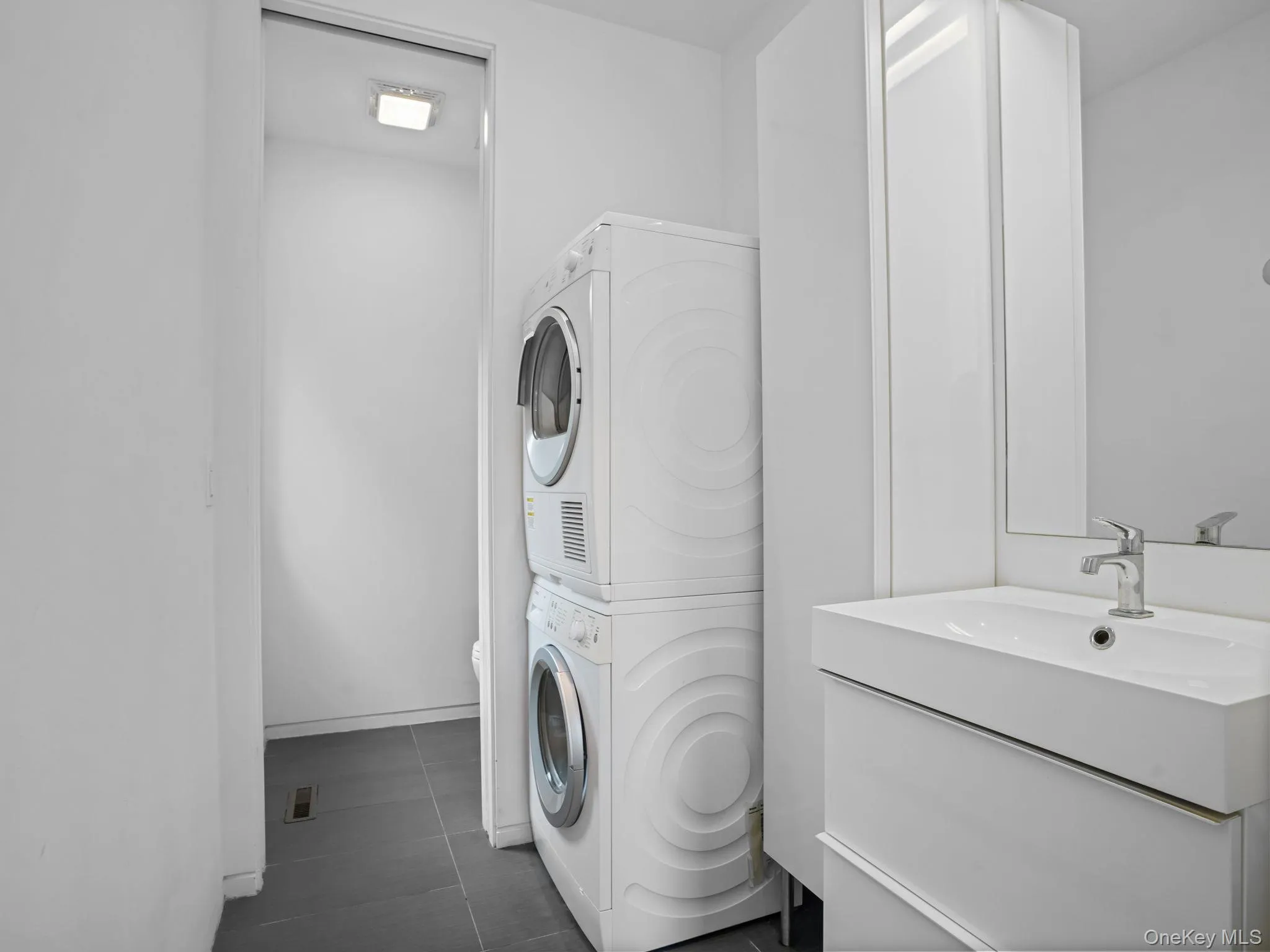 Laundry area with stacked washer and clothes dryer and dark tile patterned floors Laundry area with stacked washer and clothes dryer and dark tile patterned floors