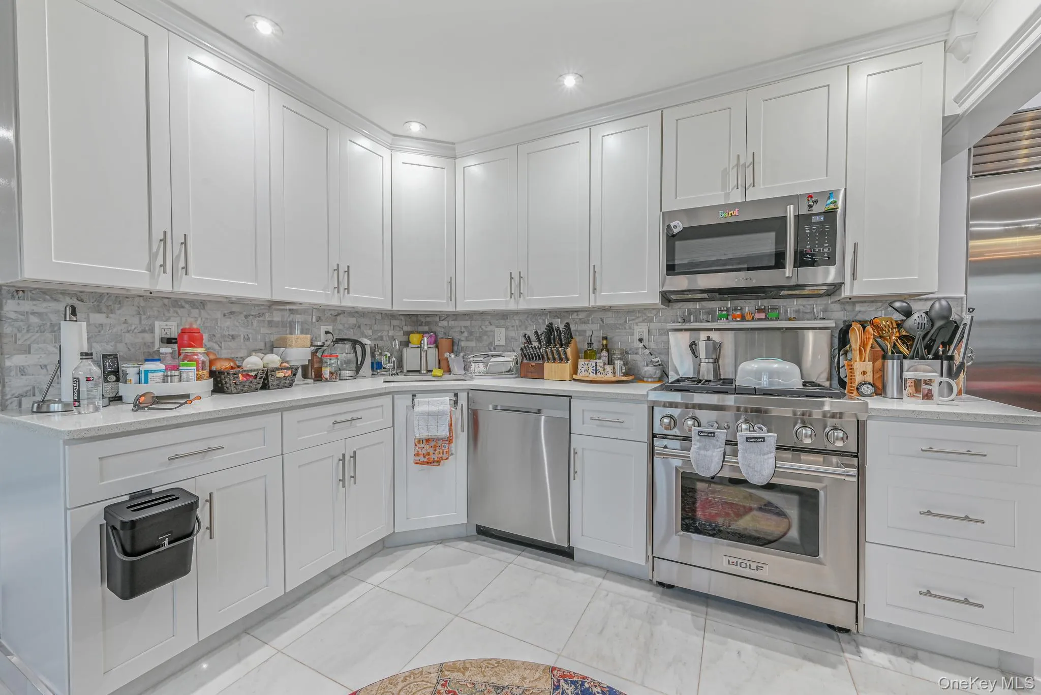Kitchen featuring high quality appliances, backsplash, light stone countertops, and white cabinetry Kitchen featuring high quality appliances, backsplash, light stone countertops, and white cabinetry