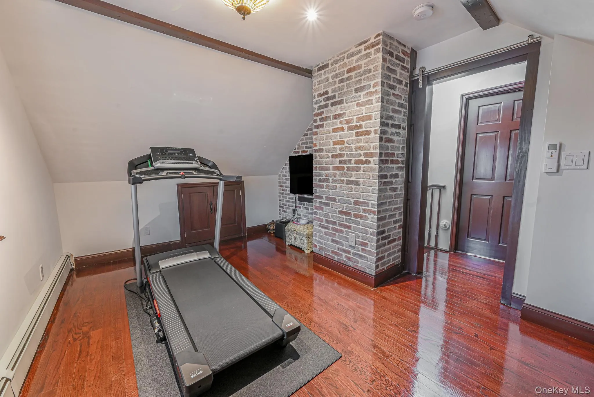 Workout room featuring vaulted ceiling, a barn door, baseboard heating, and wood finished floors Workout room featuring vaulted ceiling, a barn door, baseboard heating, and wood finished floors